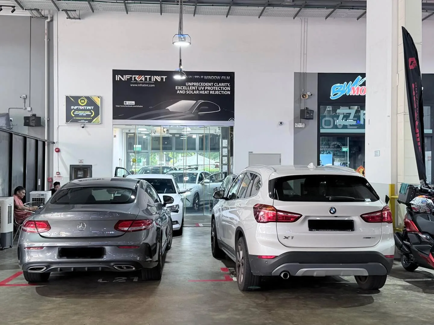 A silver Mercedes-Benz saloon and a white BMW X1 SUV parked side by side in the workshop.