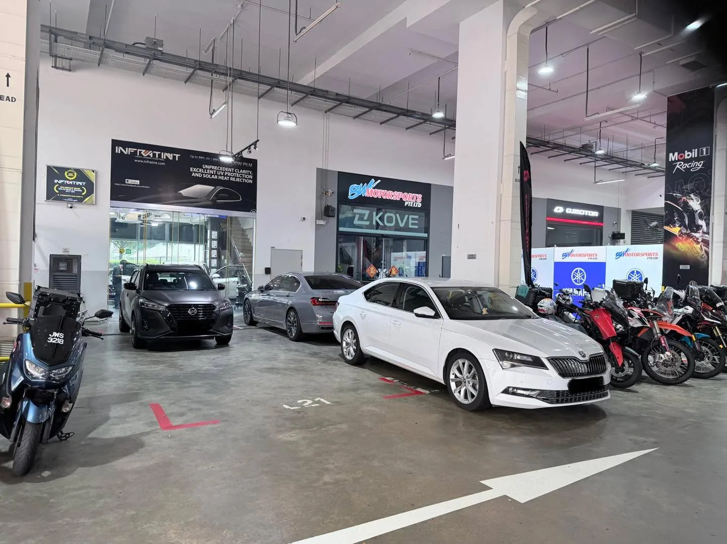 A black Mitsubishi SUV, a silver sedan, and a white Skoda saloon inside the workshop with motorcycles nearby.