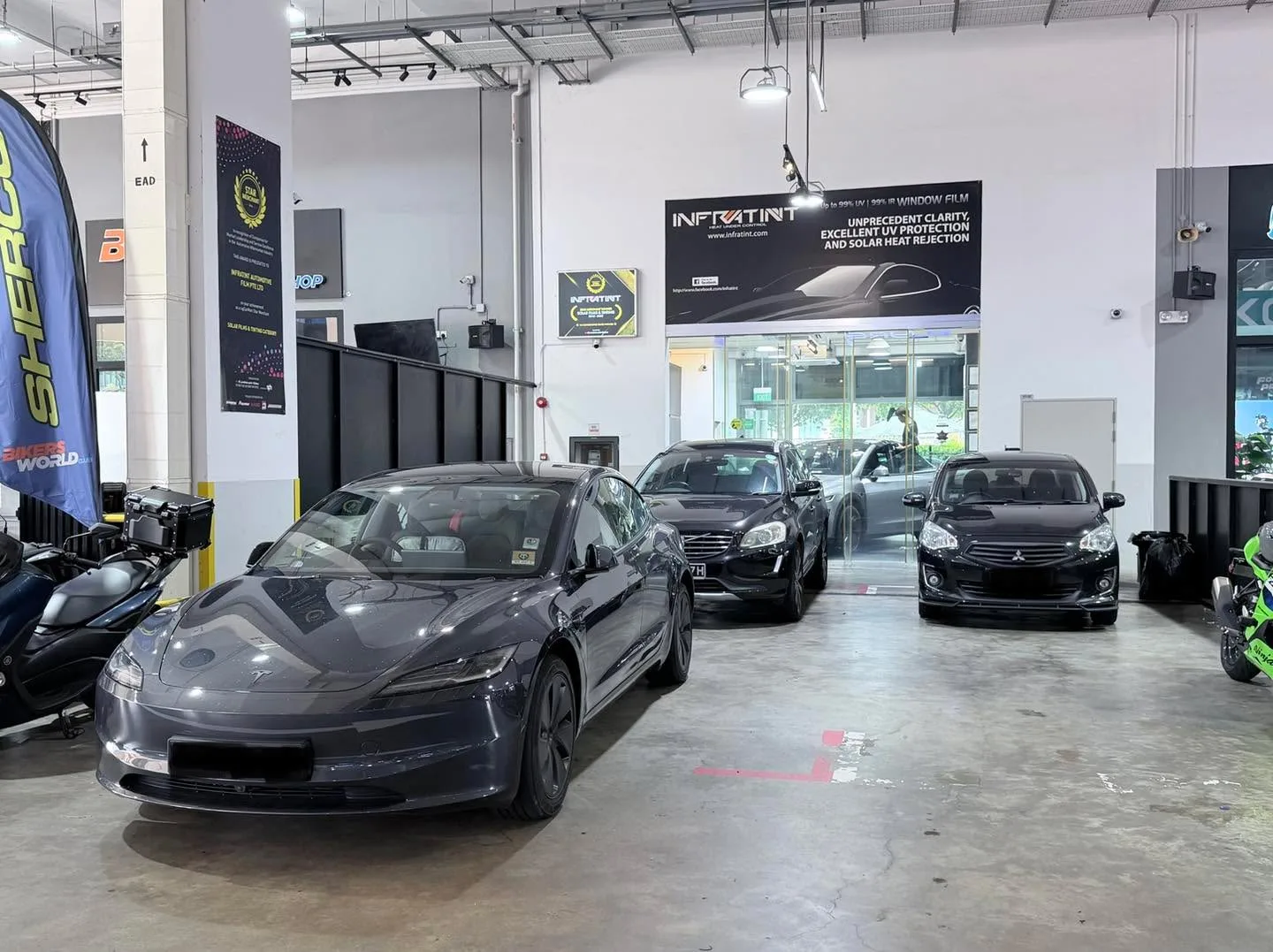 A dark grey Tesla sedan in the foreground with two black sedans behind it inside the workshop.