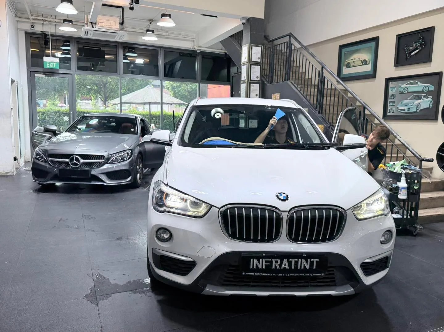 A white Tesla sedan viewed from the front with a dark Mercedes-Benz beside it inside the workshop.