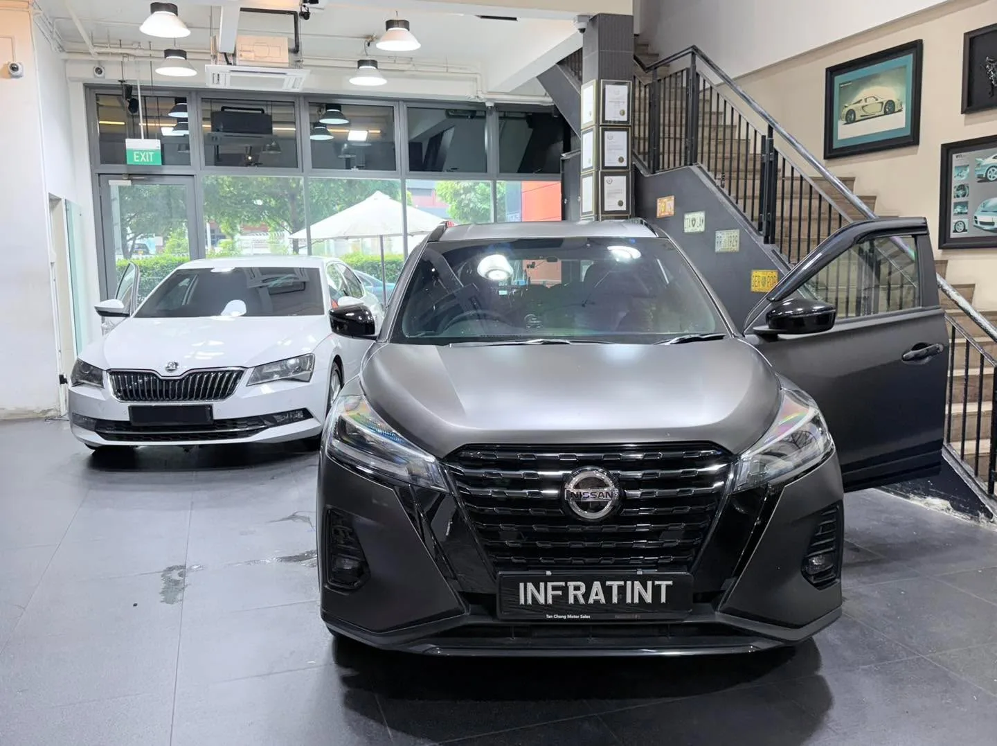 A white Skoda Superb saloon and a grey Nissan Kicks e-POWER SUV viewed from the front inside the workshop.