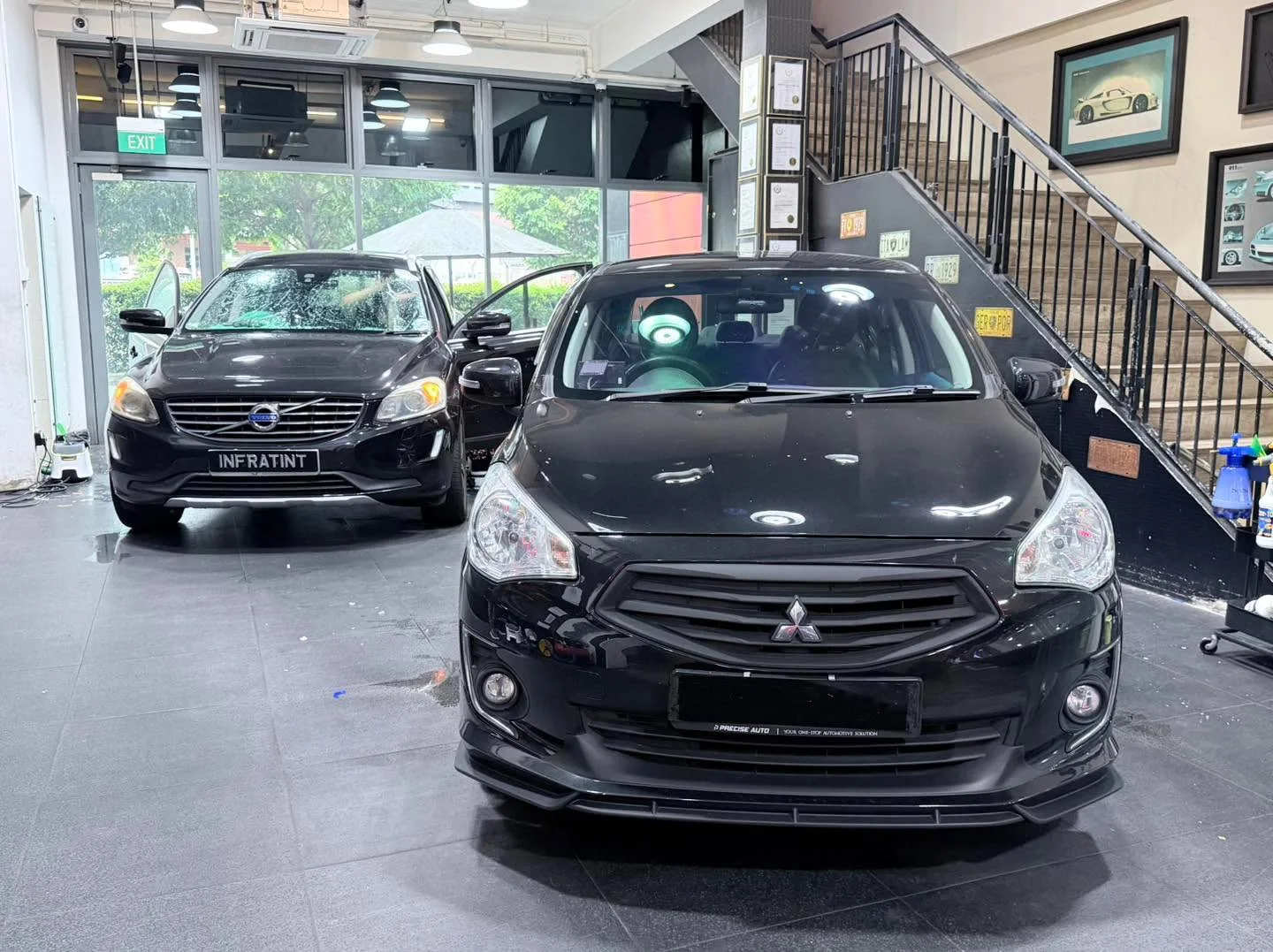 A black Nissan and a black Volvo XC60 SUV parked in the workshop.