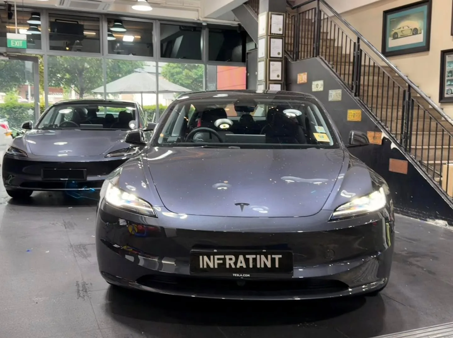 A dark grey Tesla sedan and a dark blue BMW SUV parked in the workshop near the entrance.