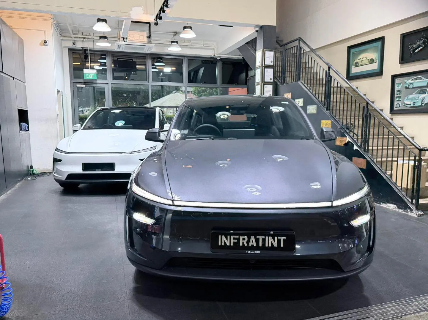A black Tesla sedan with illuminated headlights displayed in the showroom, viewed from the front.