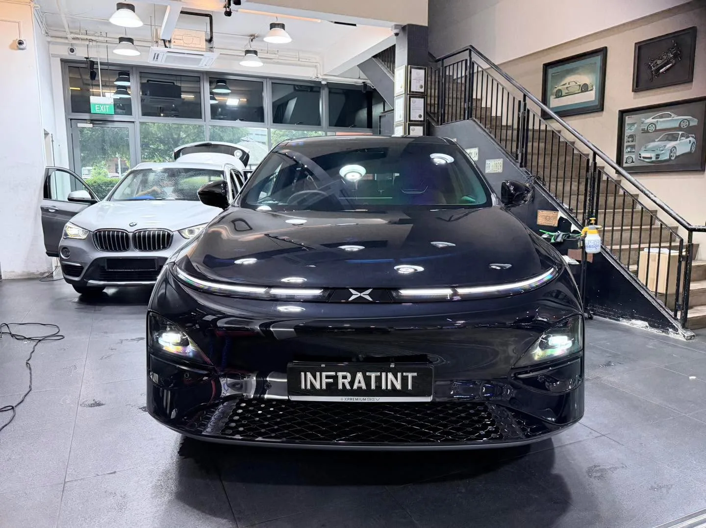 A black Tesla sedan and a white BMW X1 SUV inside the showroom, viewed from the front.