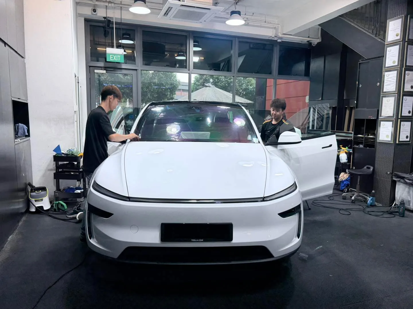 A white Tesla sedan with the door open, technicians working on the windows.