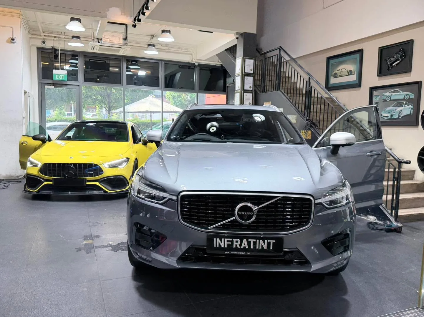 A yellow Mercedes-AMG and a silver Volvo XC60 parked side by side with an open car door visible.