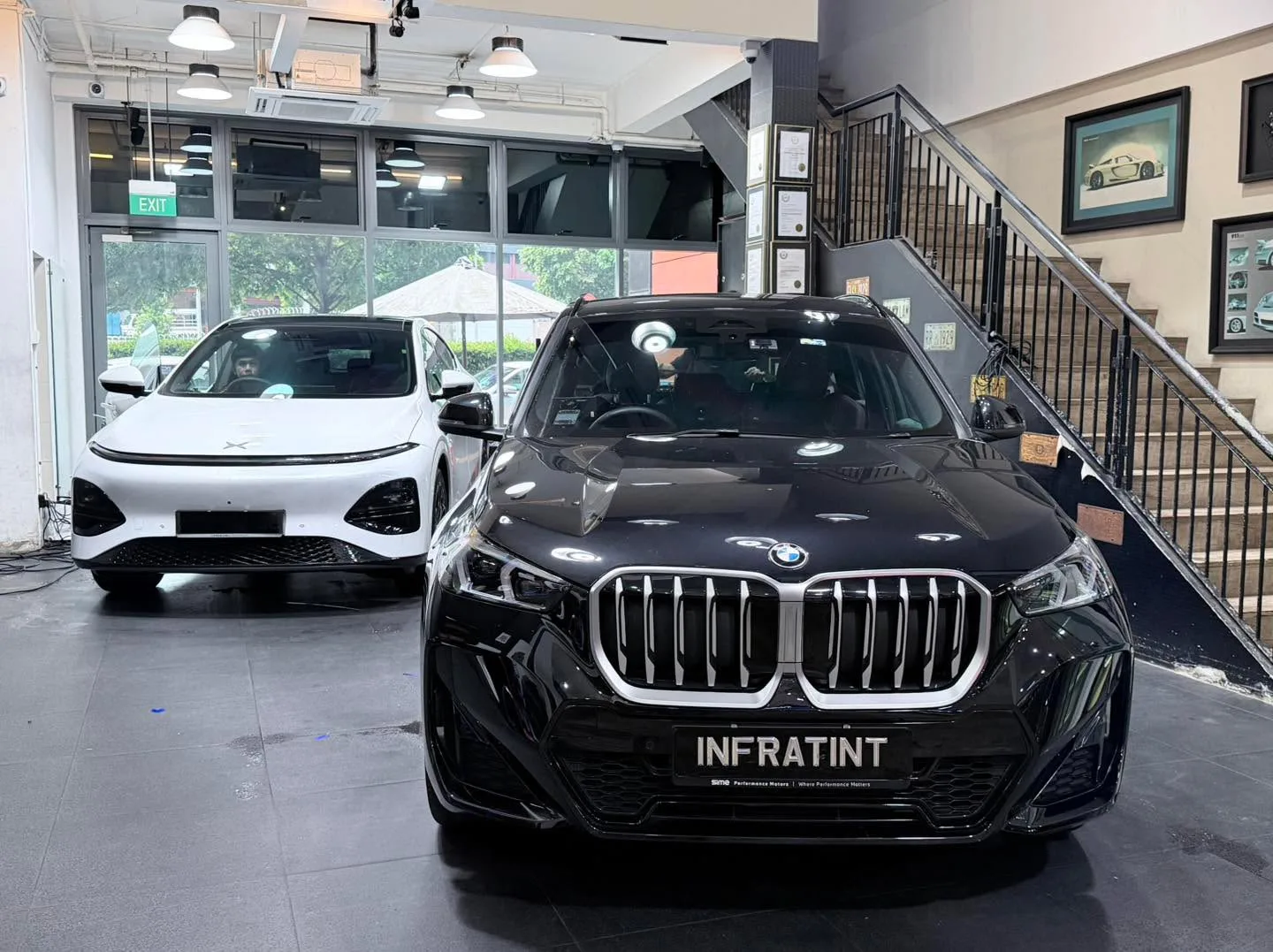 A black BMW X4 with an open door, next to a white car, inside the workshop.