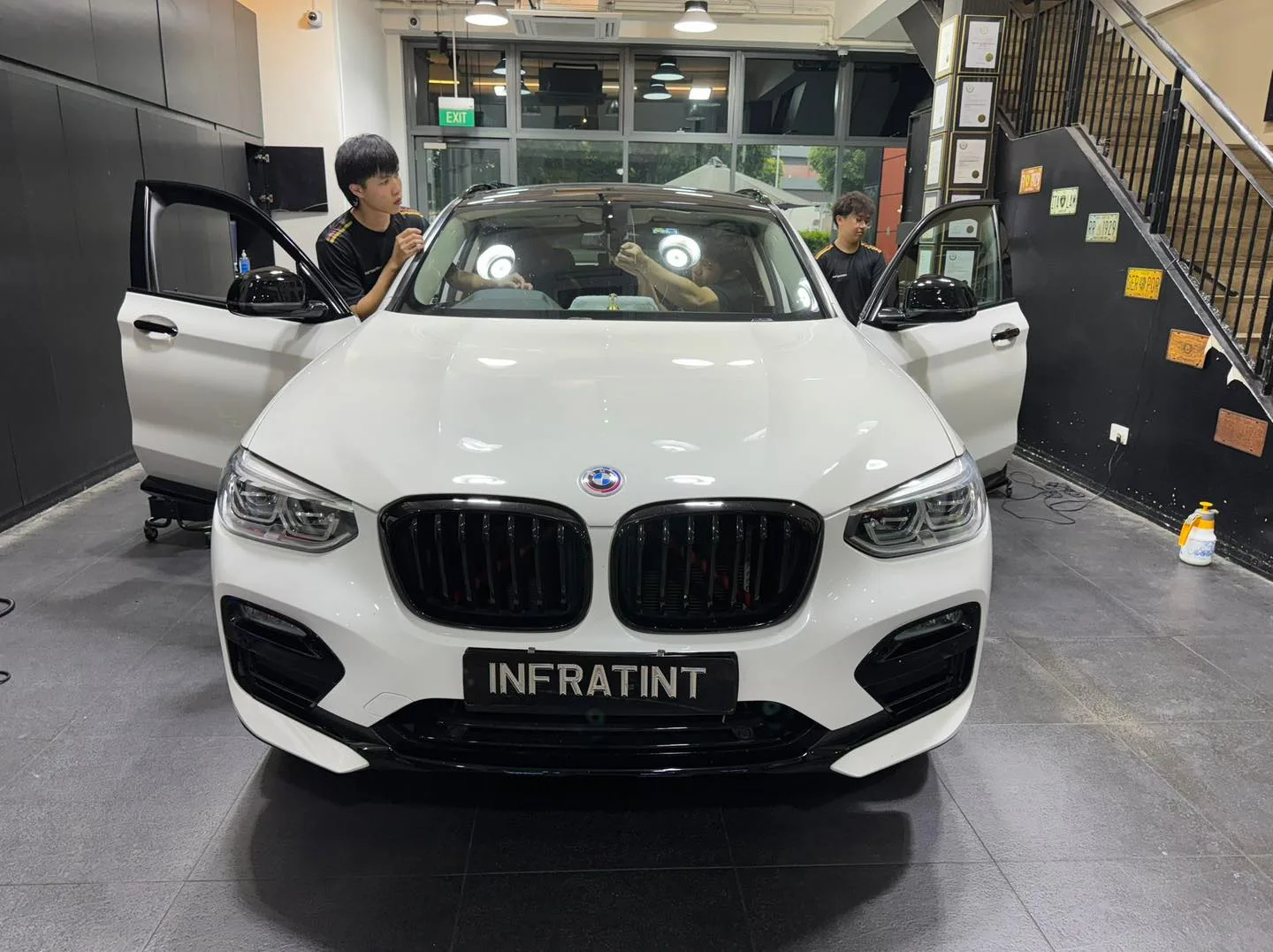 A white BMW viewed head-on with open doors, being worked on inside the workshop.