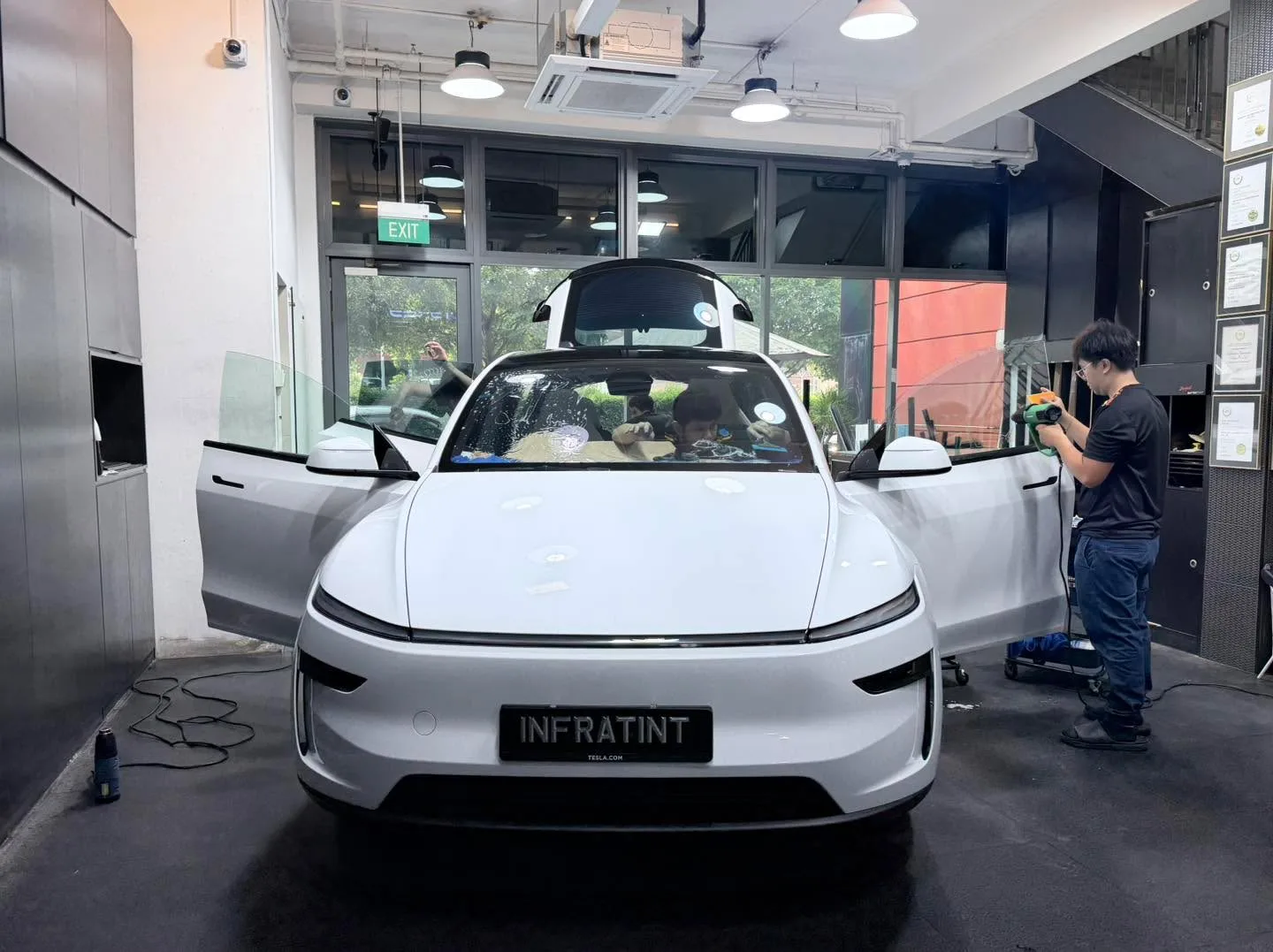 A white Tesla with gull-wing doors open, being serviced by technicians inside the workshop.