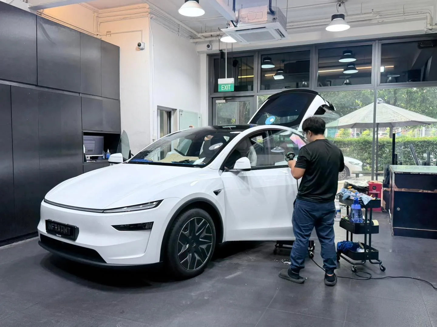 A white Tesla with open door, technician working on window tinting outside the workshop.