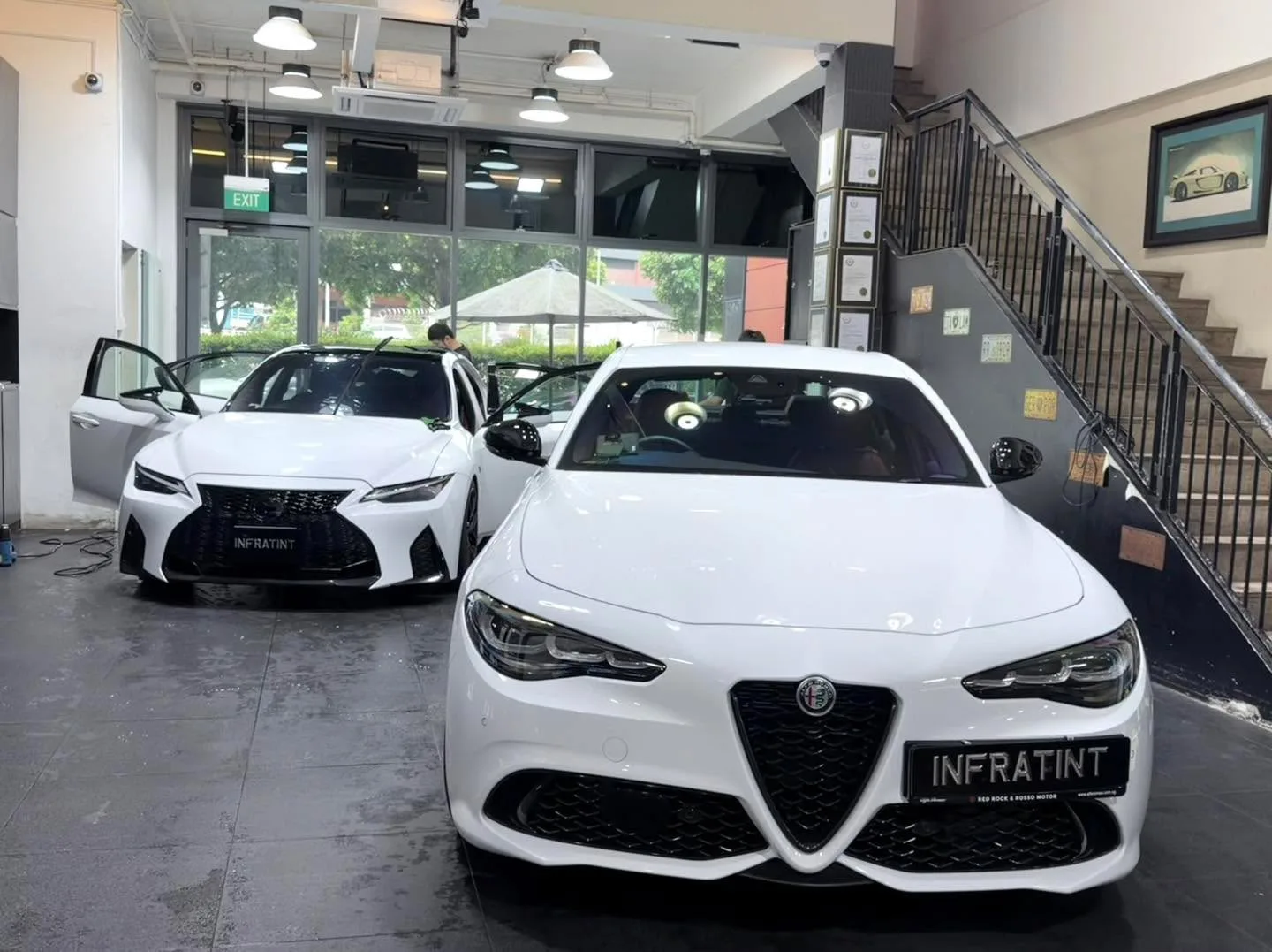 A white Alfa Romeo Giulia sedan parked indoors with a black Lexus sedan to its left.