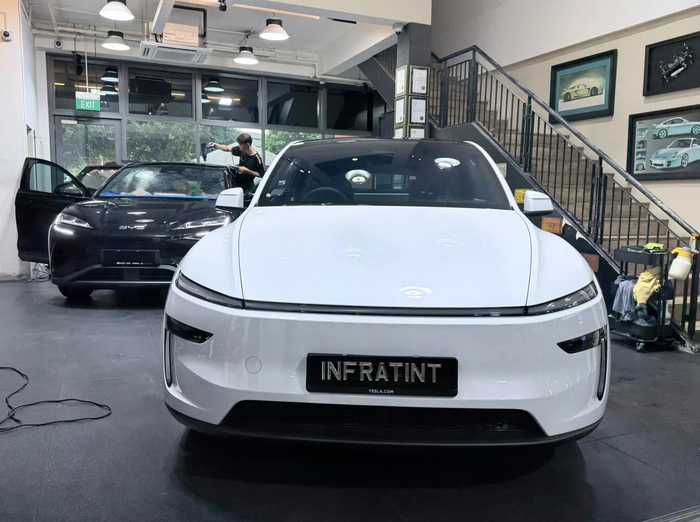 A white Tesla sedan undergoing window tinting work indoors.