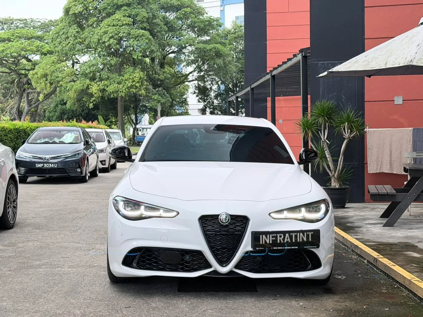 White Alfa Romeo Giulia parked at Infratint workshop, front view showing distinctive grille and headlights.