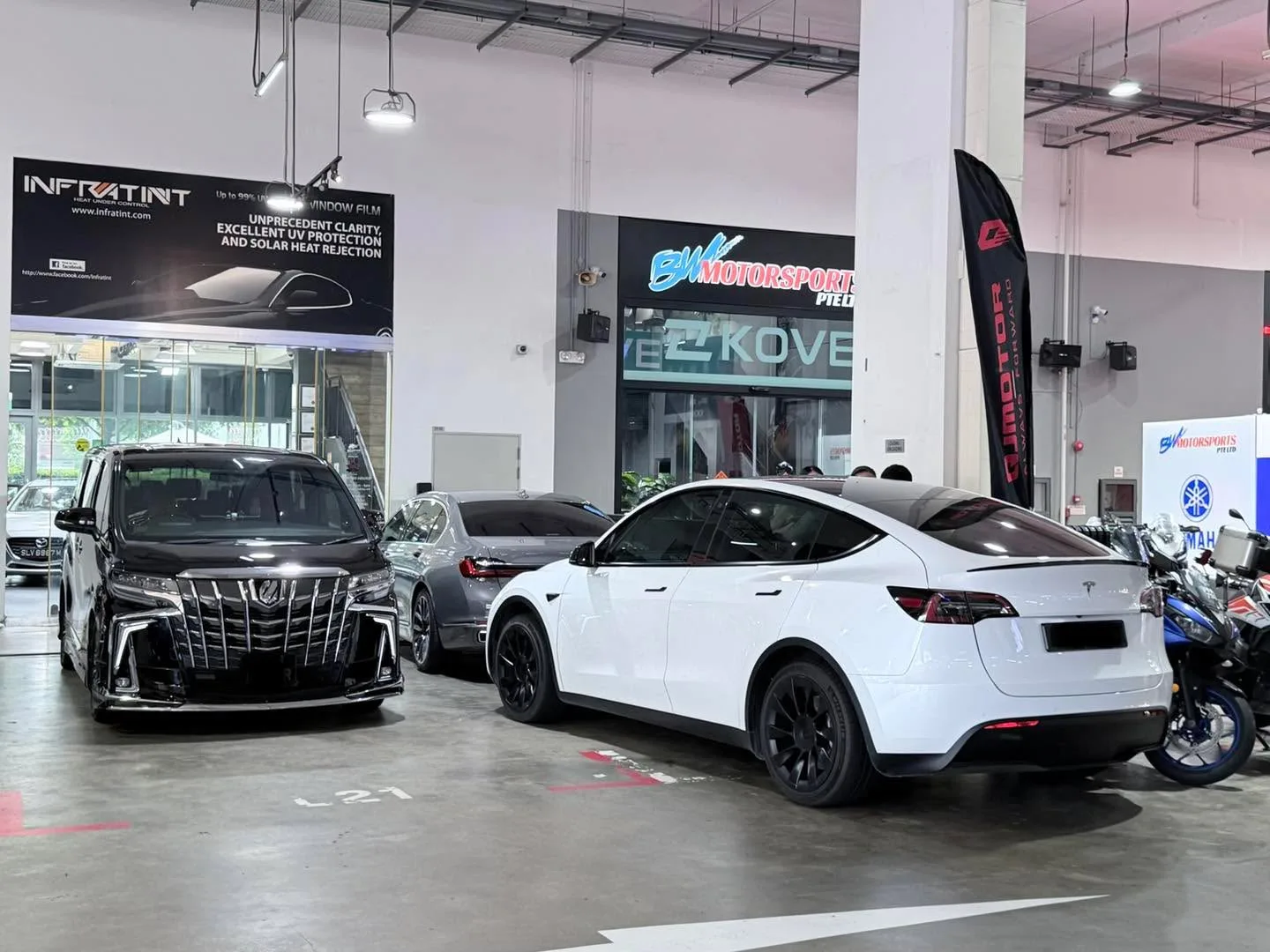 A white Tesla Model Y, black Toyota Alphard and other cars in the workshop.
