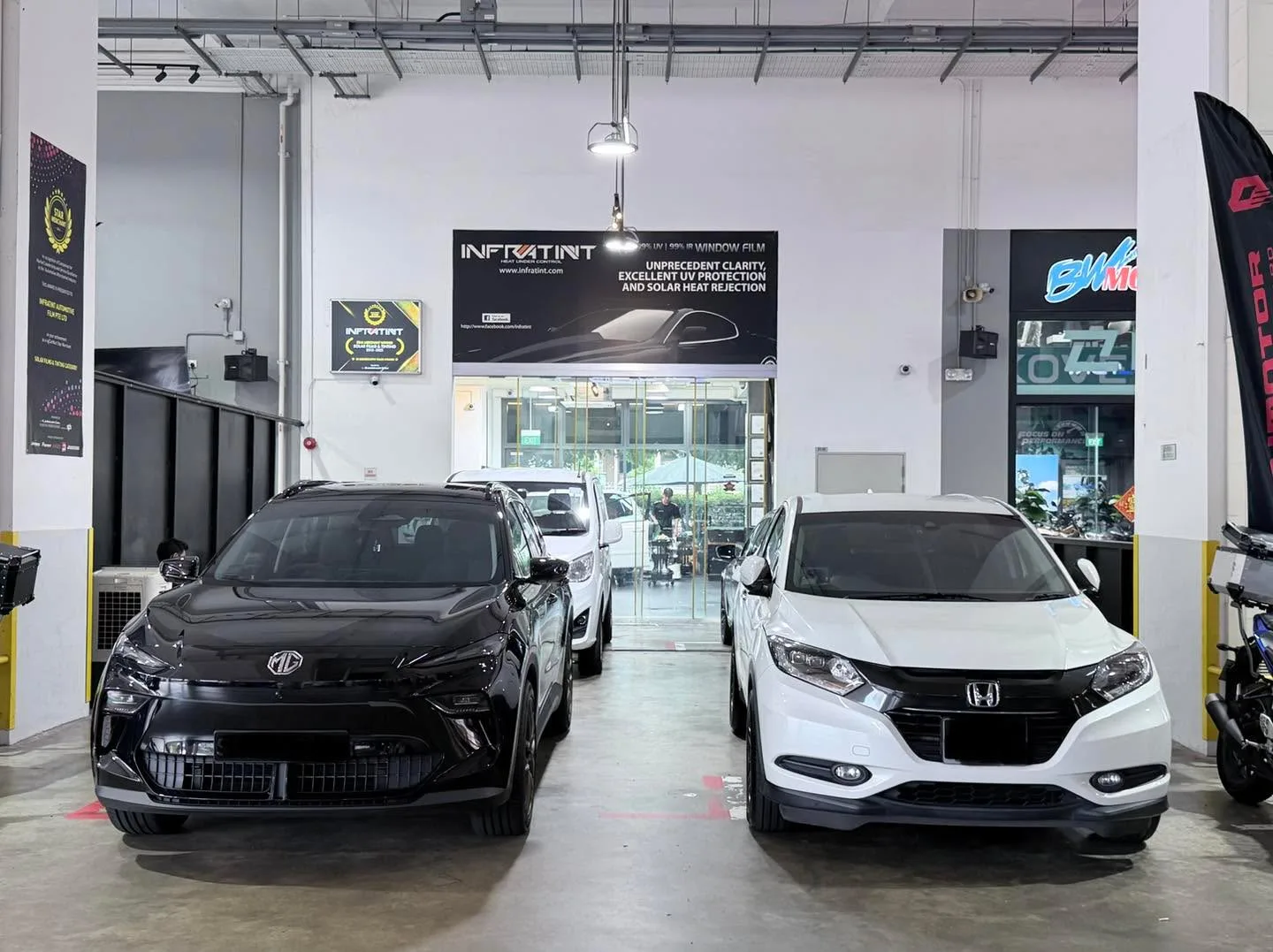 A black MG5 sedan and white Honda Vezel SUV parked indoors.