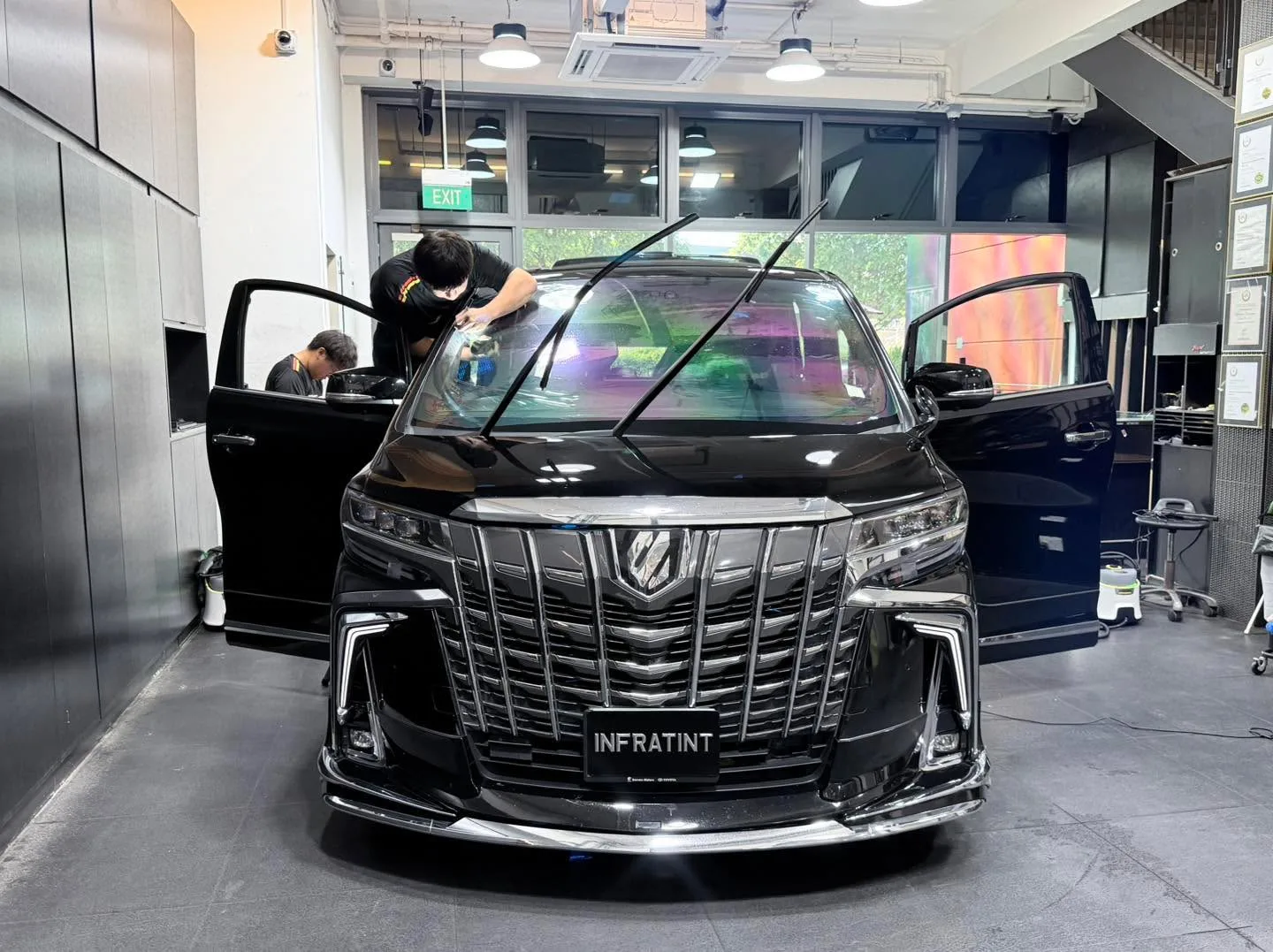 A black Toyota Alphard minivan with doors open, technician applying film to the windows.