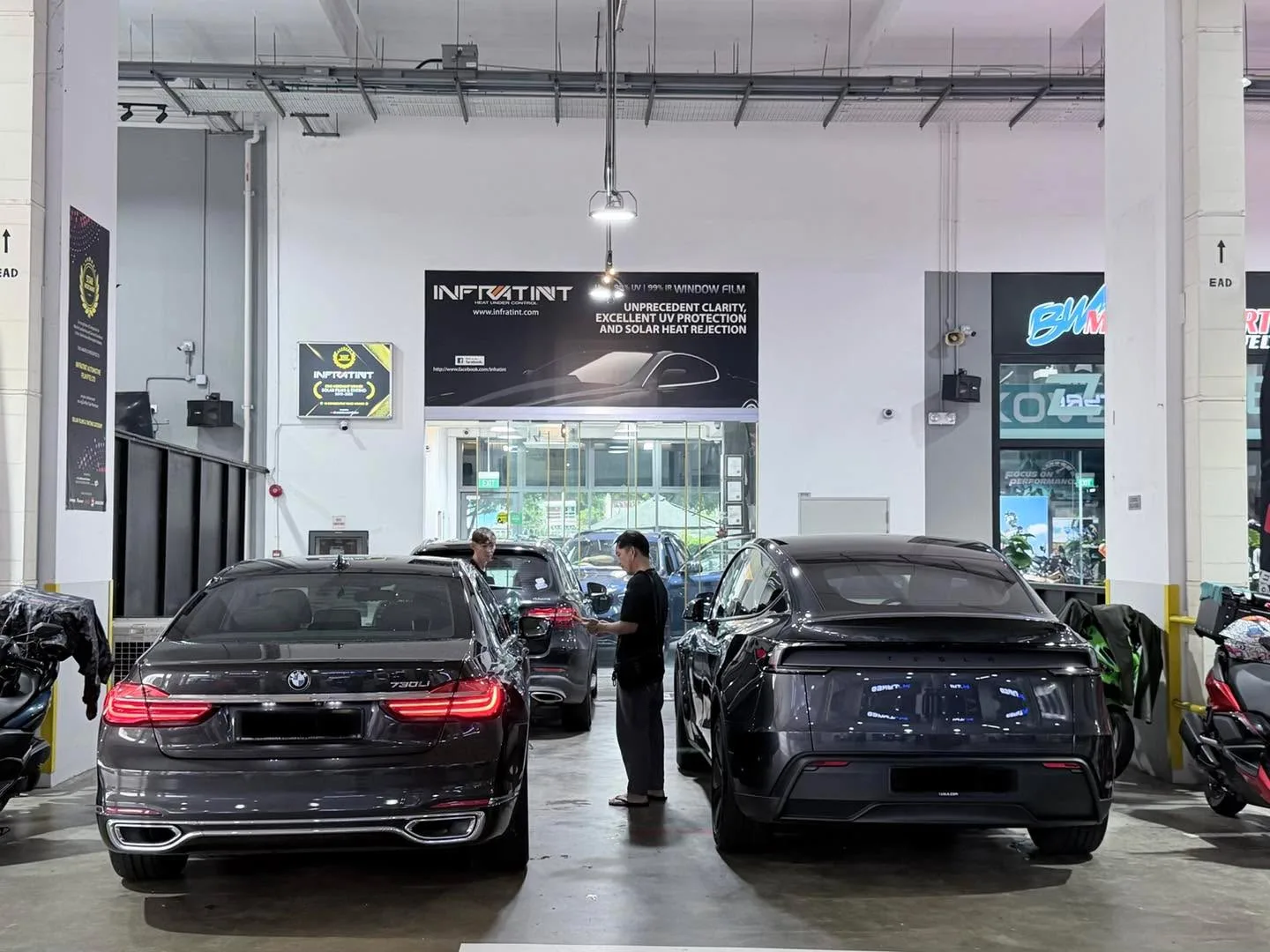A black BMW 730 sedan and a black coupe parked in the Infratint workshop.