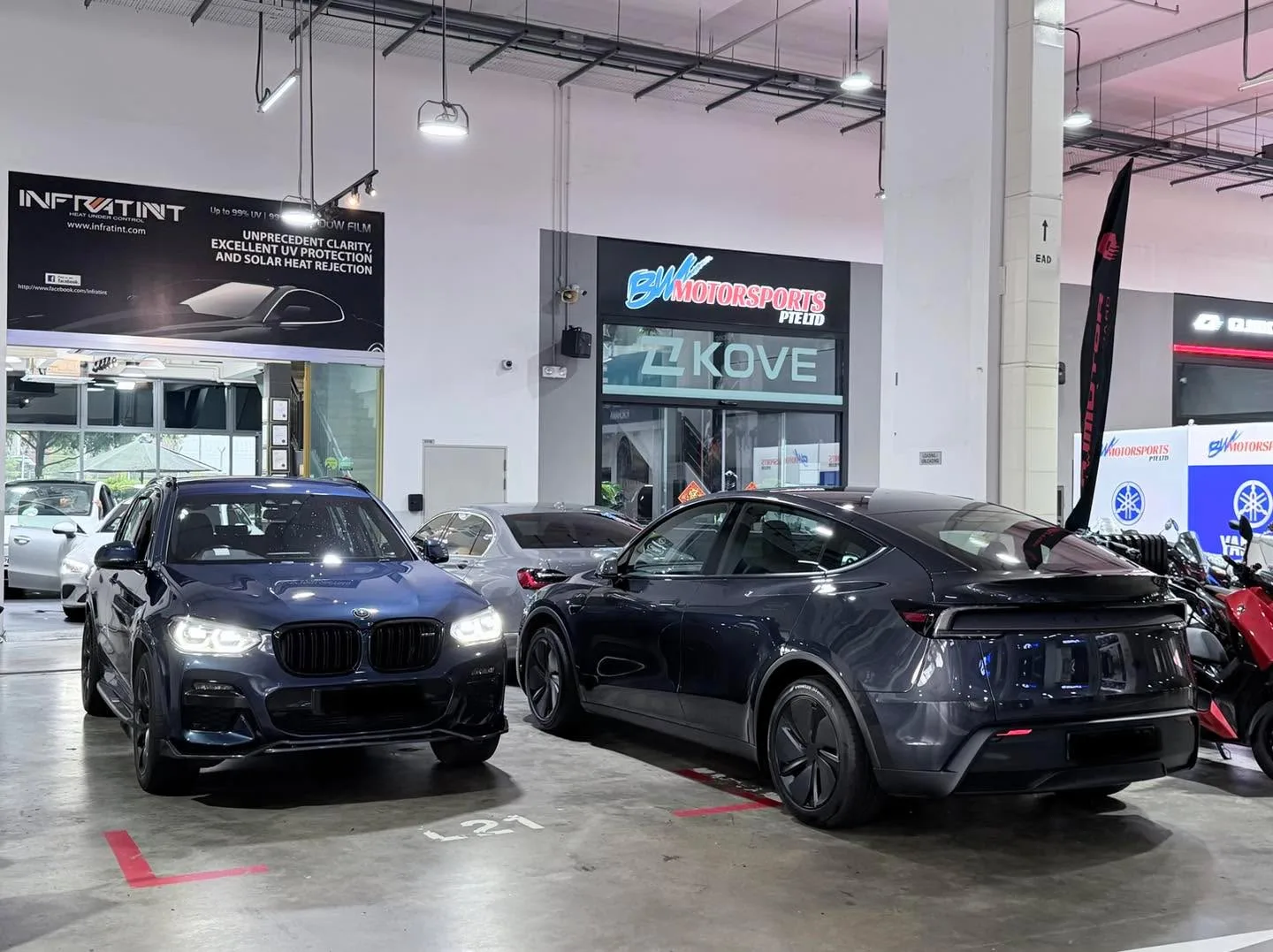 A dark blue BMW X3 SUV and a black electric car parked indoors beside shop fronts.