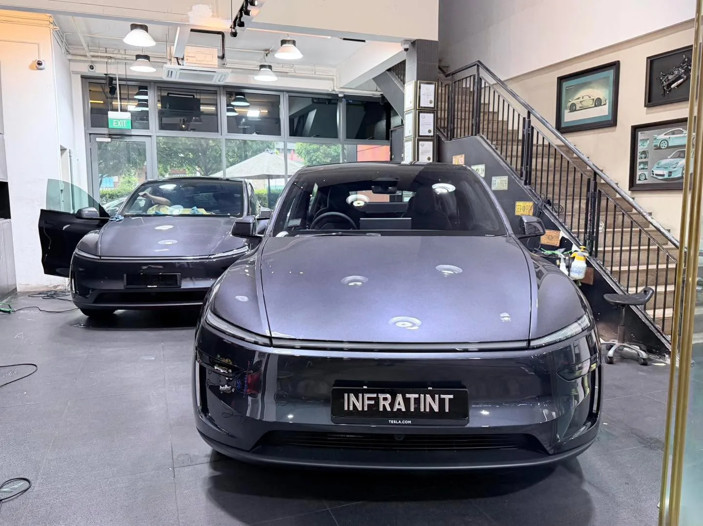 A silver Tesla Model Y hatchback with doors open, viewed from the front in a workshop.