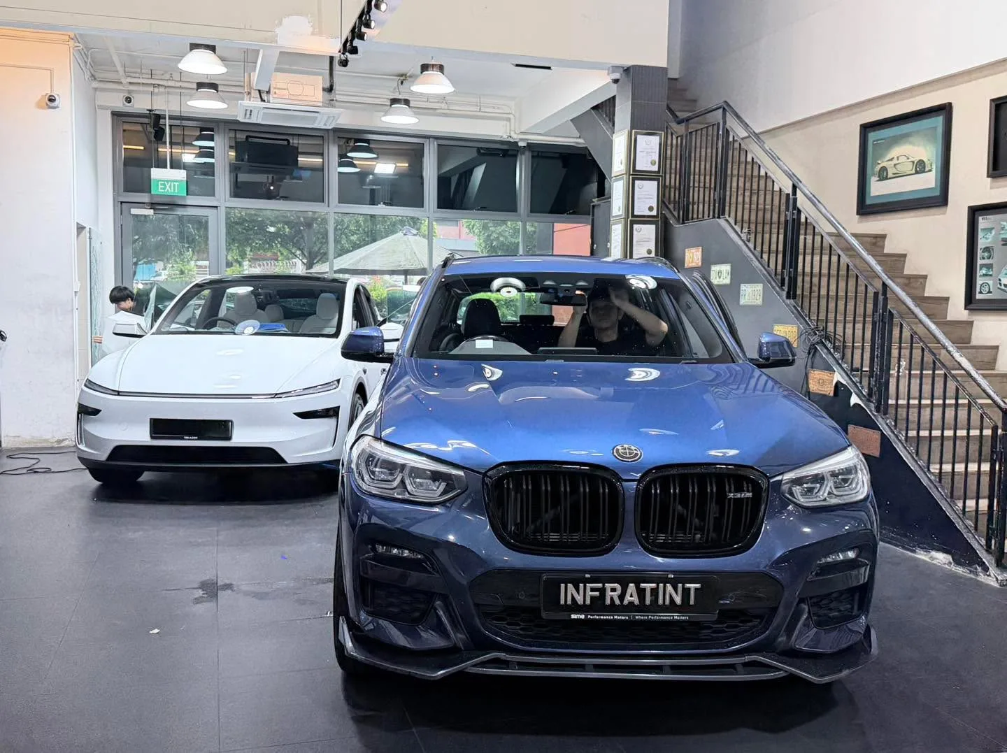 A blue BMW X3 SUV and a silver sedan parked in a workshop with a white door visible.