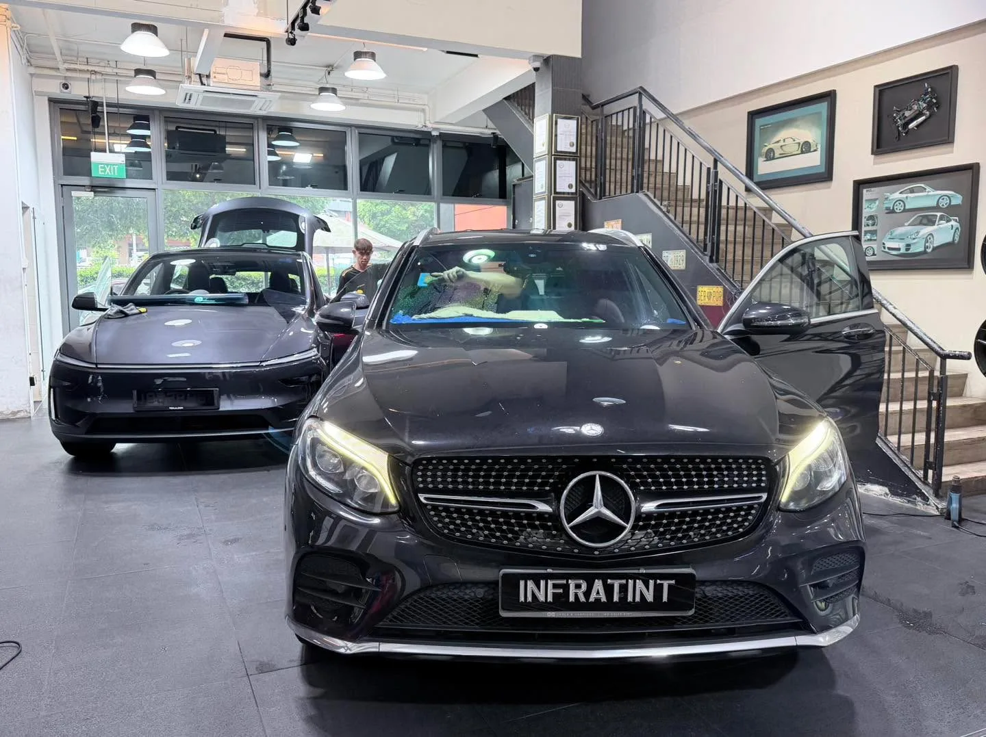 A black Mercedes-Benz GLC SUV with doors open in a workshop next to other vehicles.