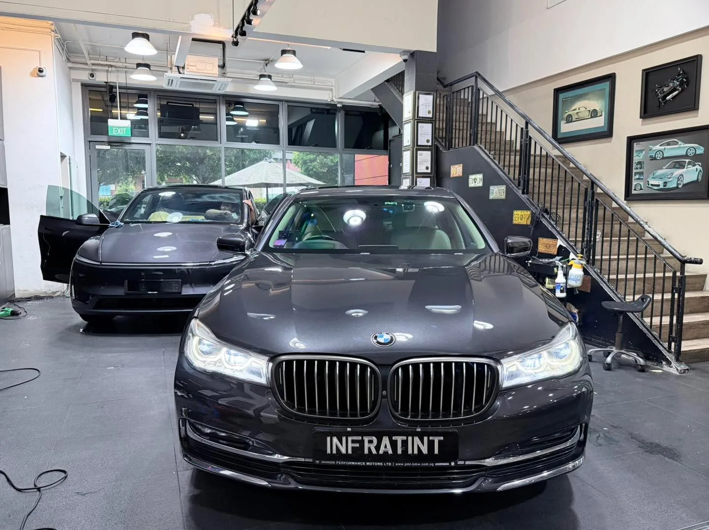 A silver BMW hatchback parked in front with another vehicle behind, doors open for tinting.