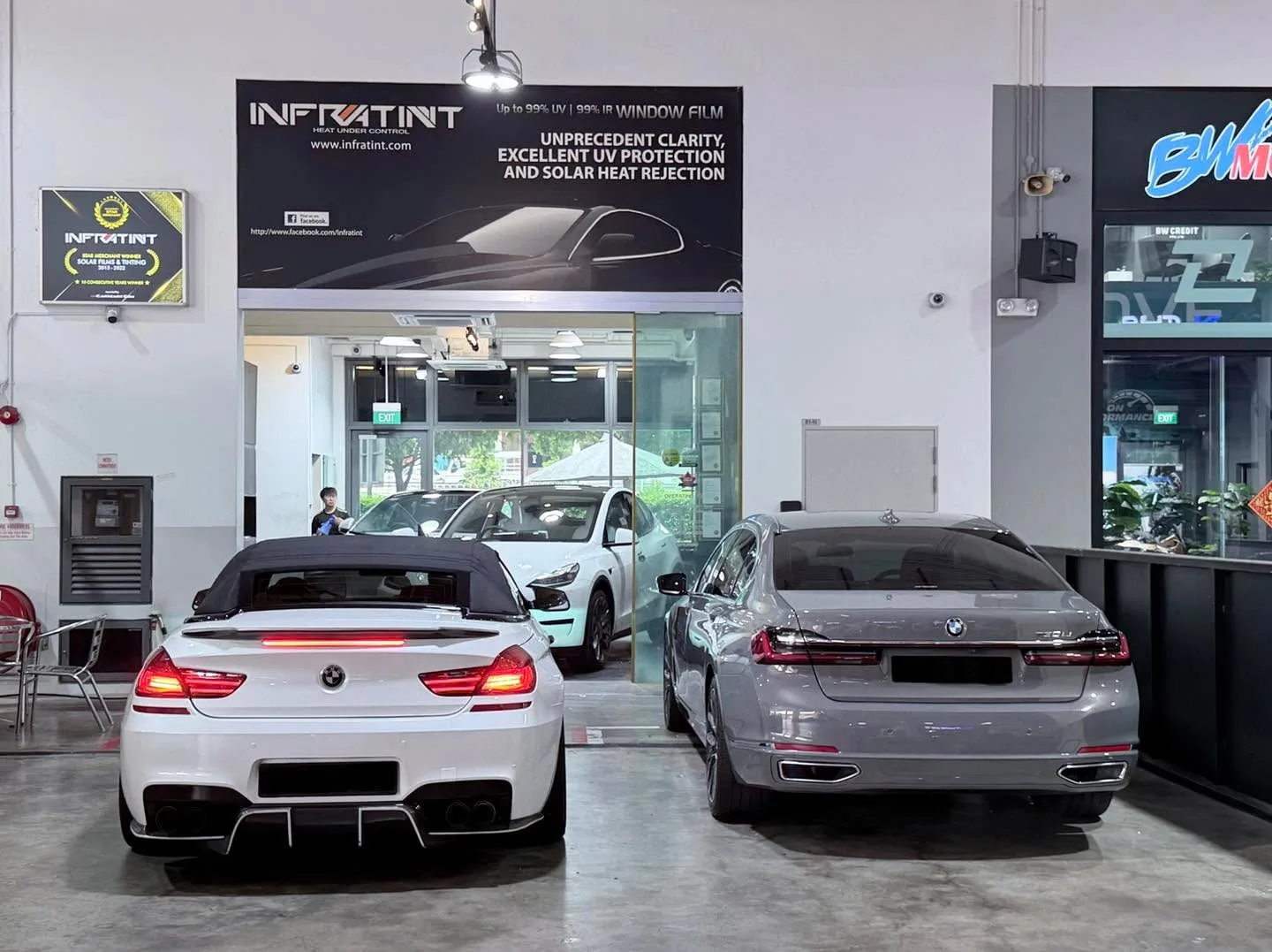 A white BMW M6 and a silver BMW sedan parked front-to-back in the workshop.