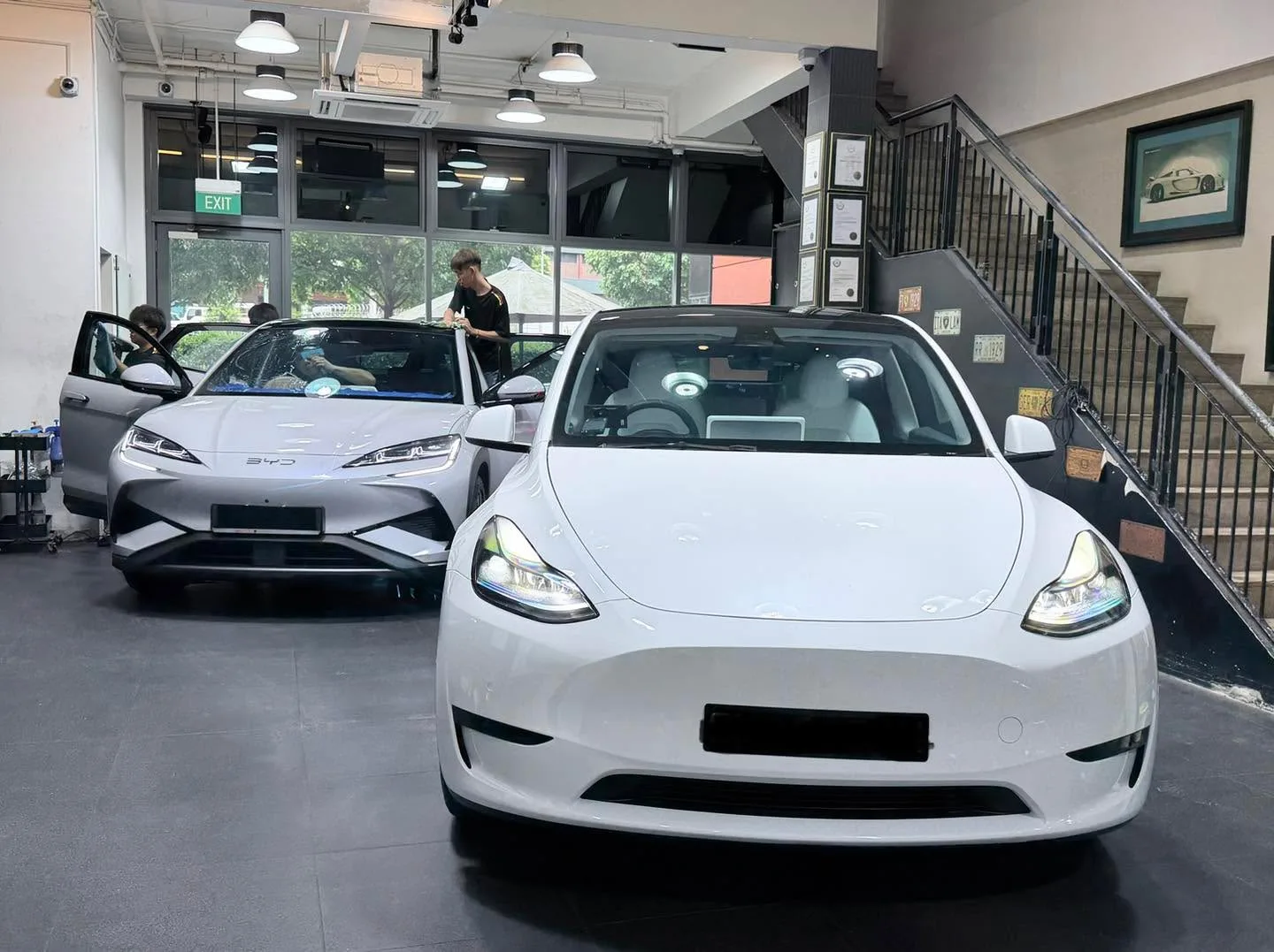 A white Tesla sedan and a silver Tesla sedan parked in the workshop with staff attending to them.