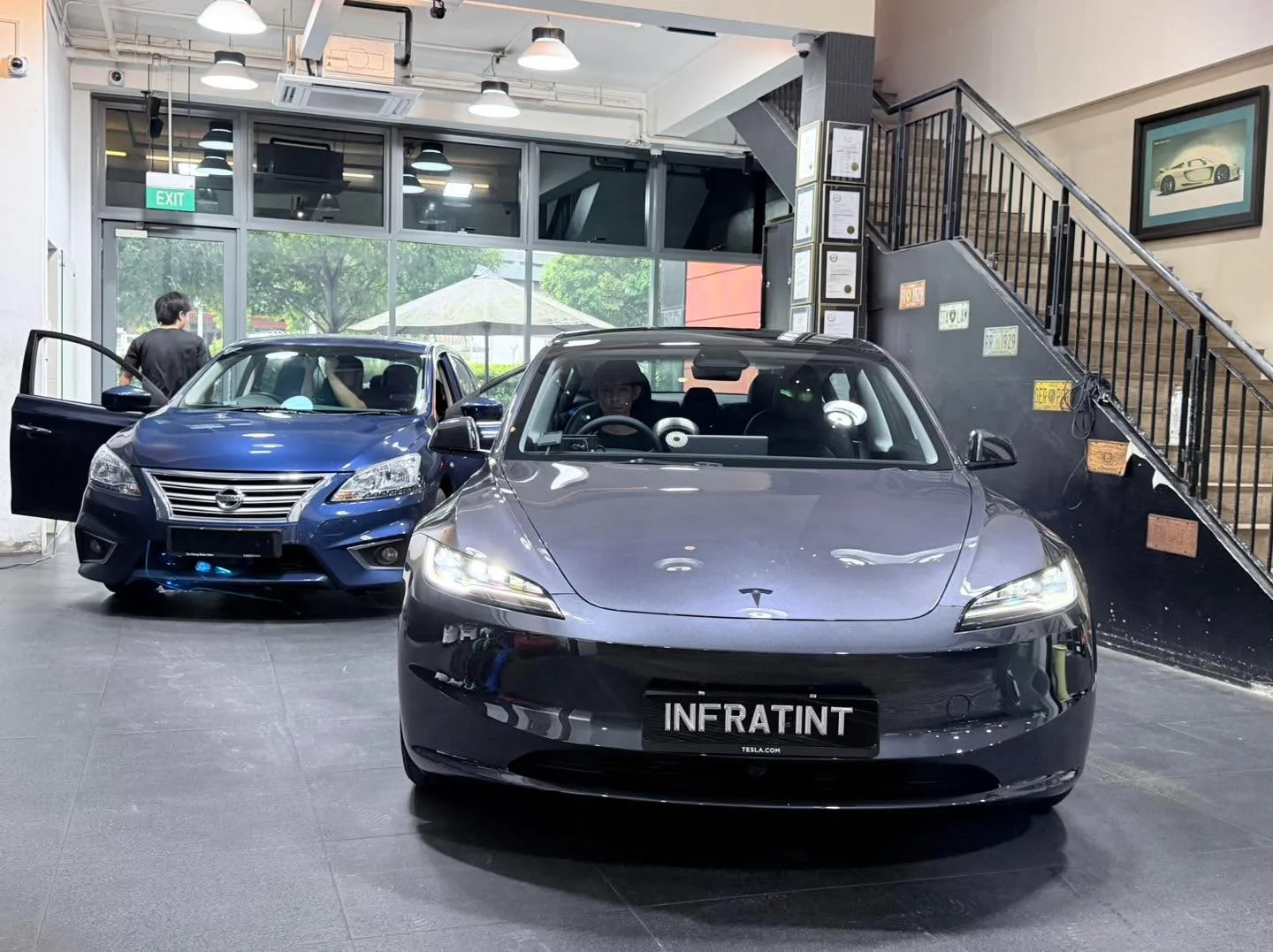 A blue Nissan Sylphy and a dark-coloured Tesla sedan parked in the workshop.