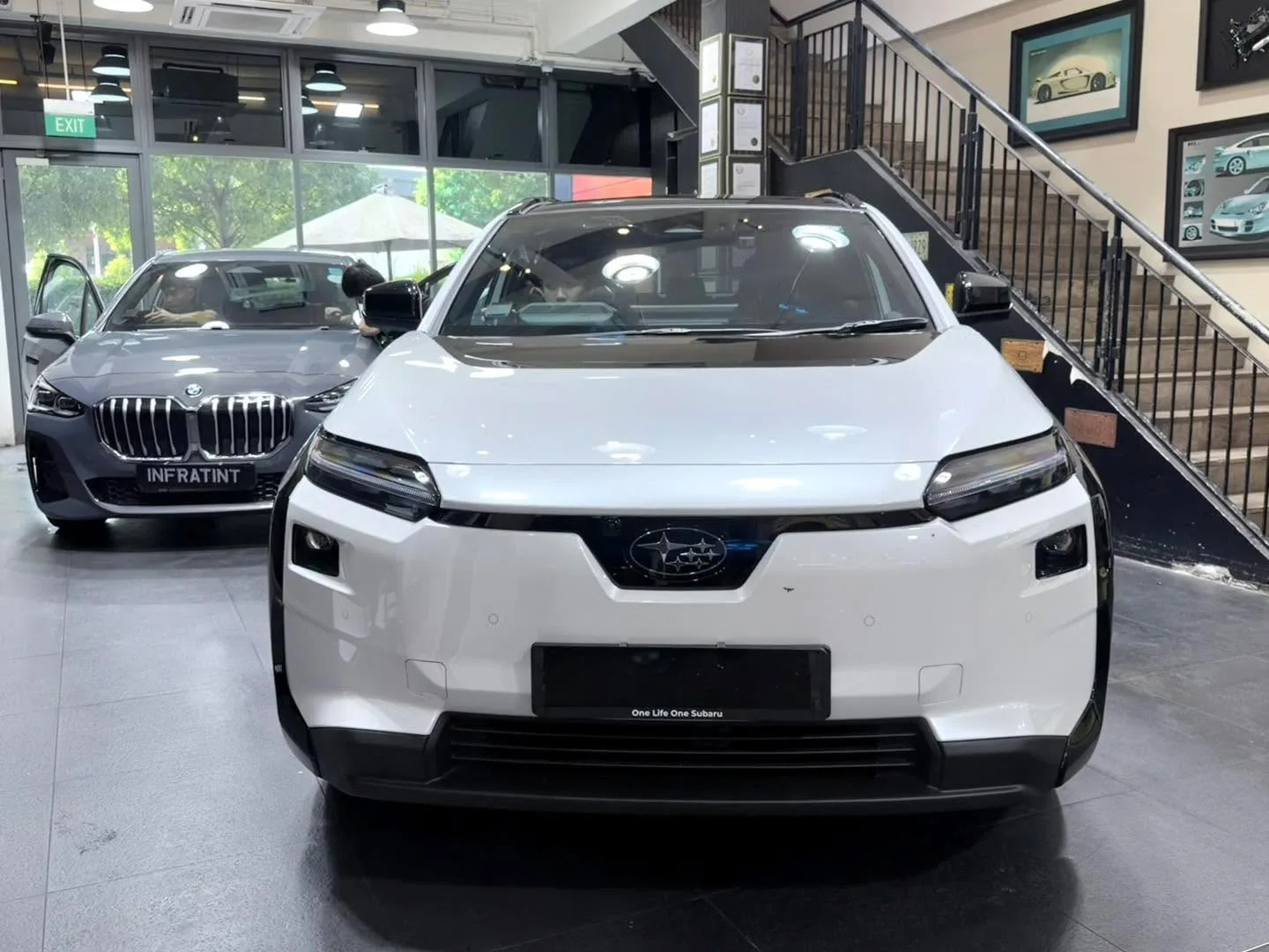 A white Subaru Solterra and a grey BMW with distinctive front grille in the workshop showroom.