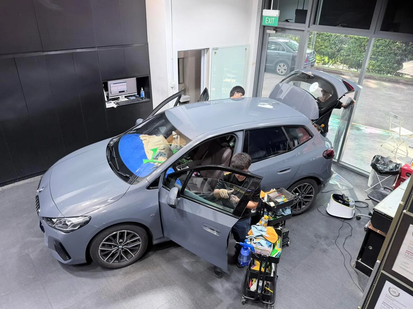 A grey hatchback with doors open, technicians applying tint to the front and rear windows.