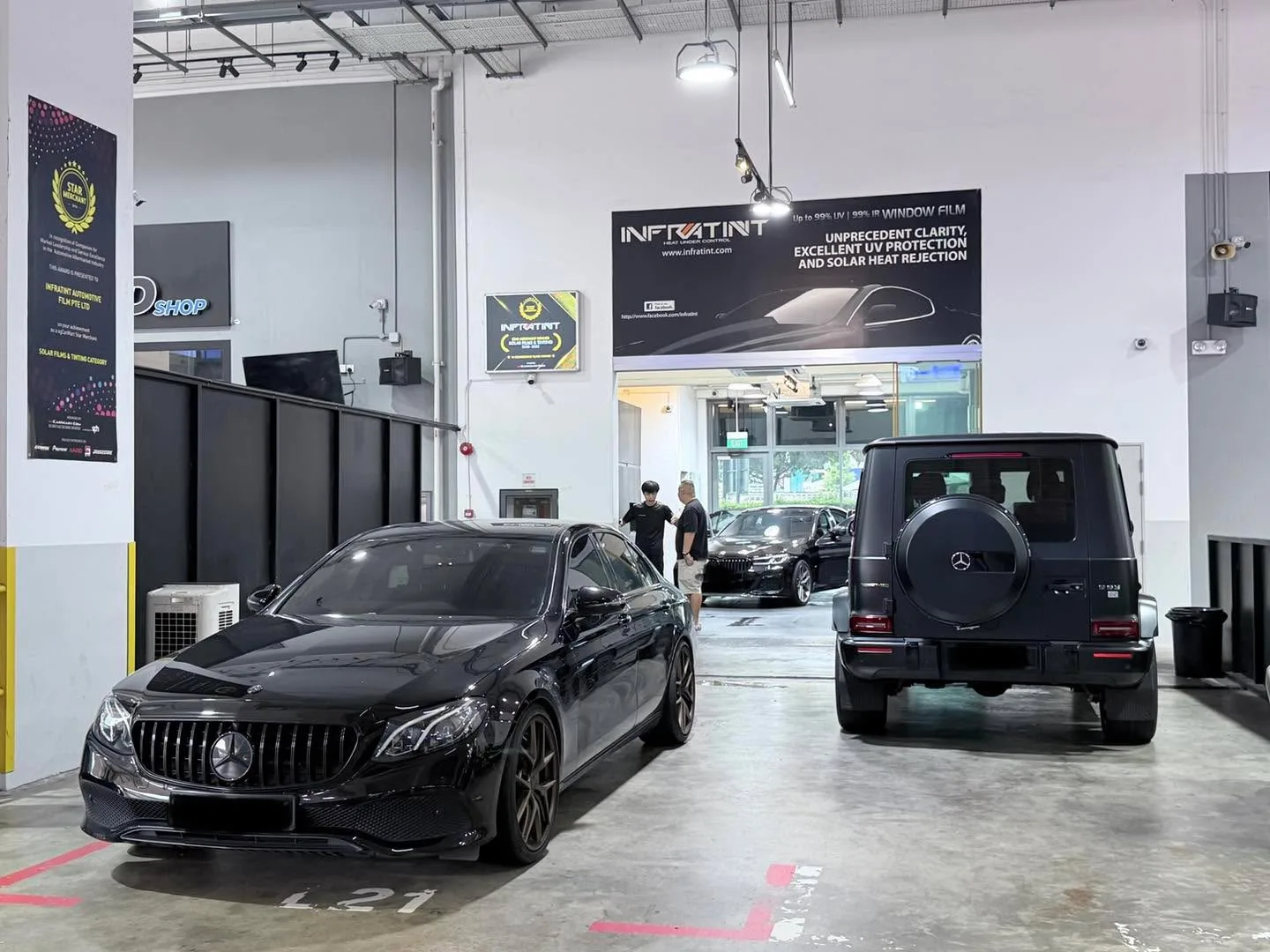 A black Mercedes-Benz G-Class SUV and a black Mercedes-Benz sedan in the Infratint workshop with staff nearby.