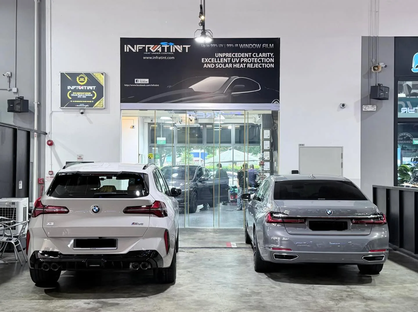 A white BMW X3 SUV and a silver BMW sedan parked facing the glass entrance of the workshop.