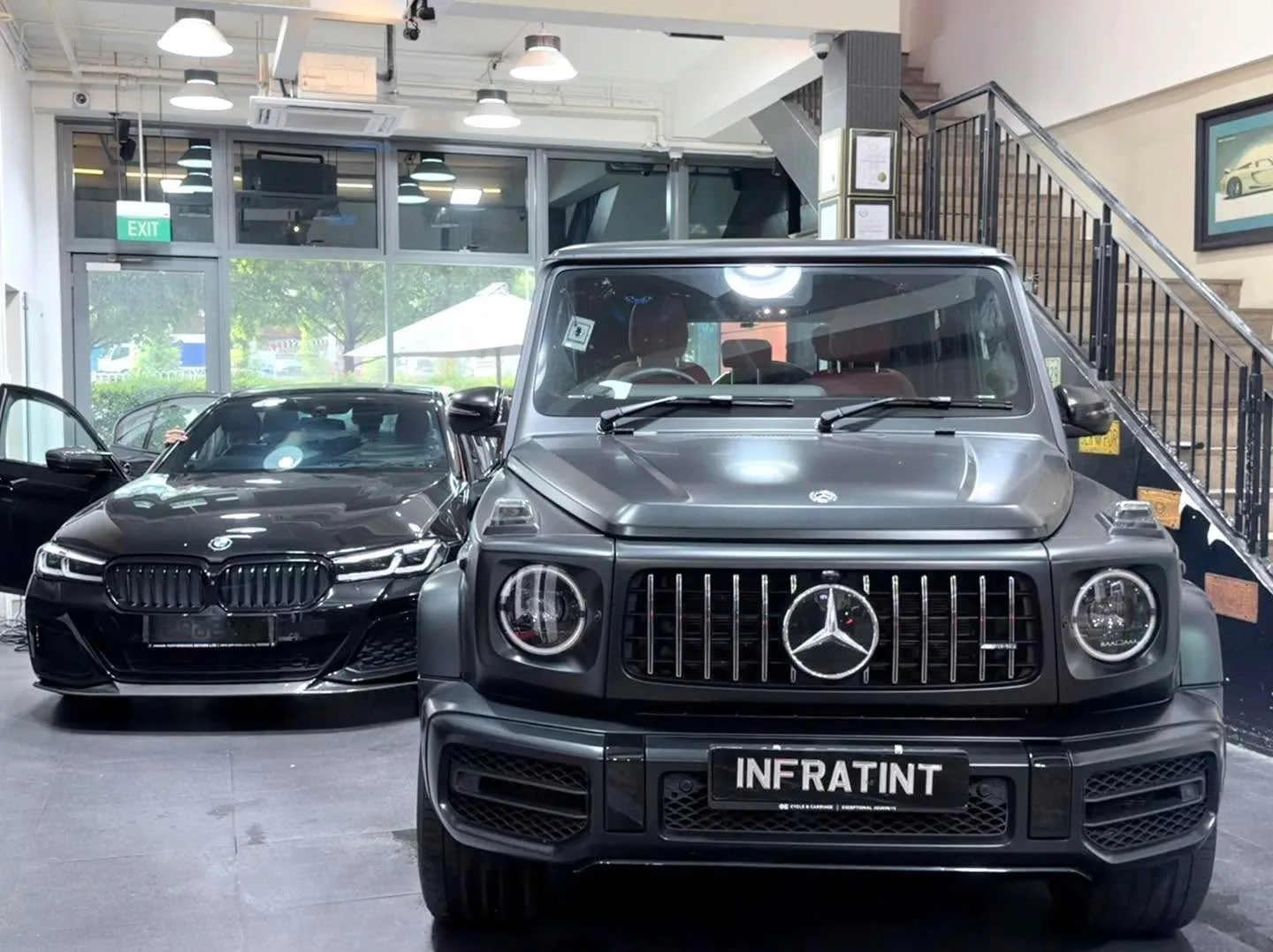 A black Mercedes-Benz G-Class and a black BMW sedan parked inside the workshop, with an Infratint banner visible.