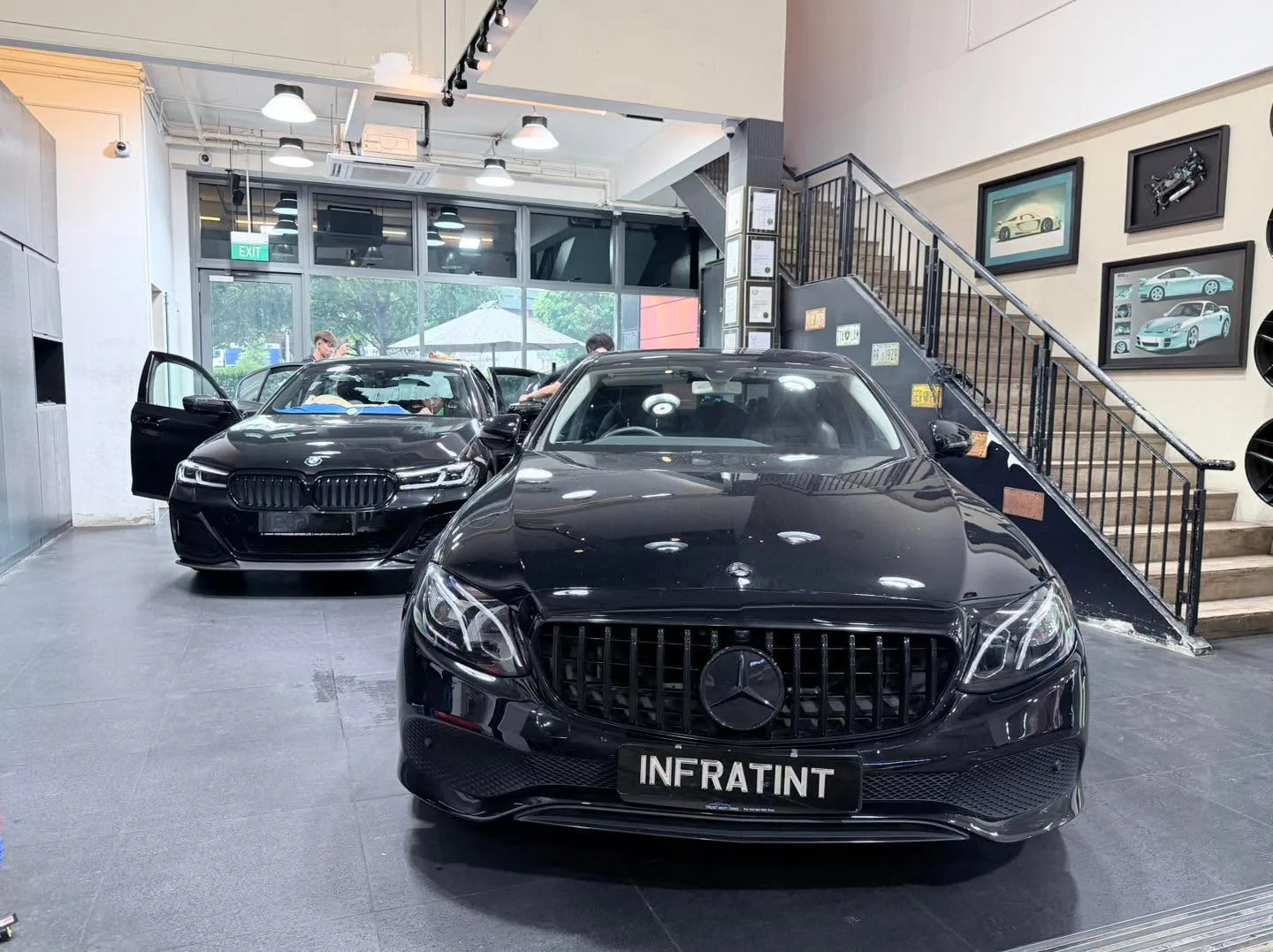 A black Mercedes-Benz CLA sedan and a black BMW sedan parked indoors with staff visible in the background.
