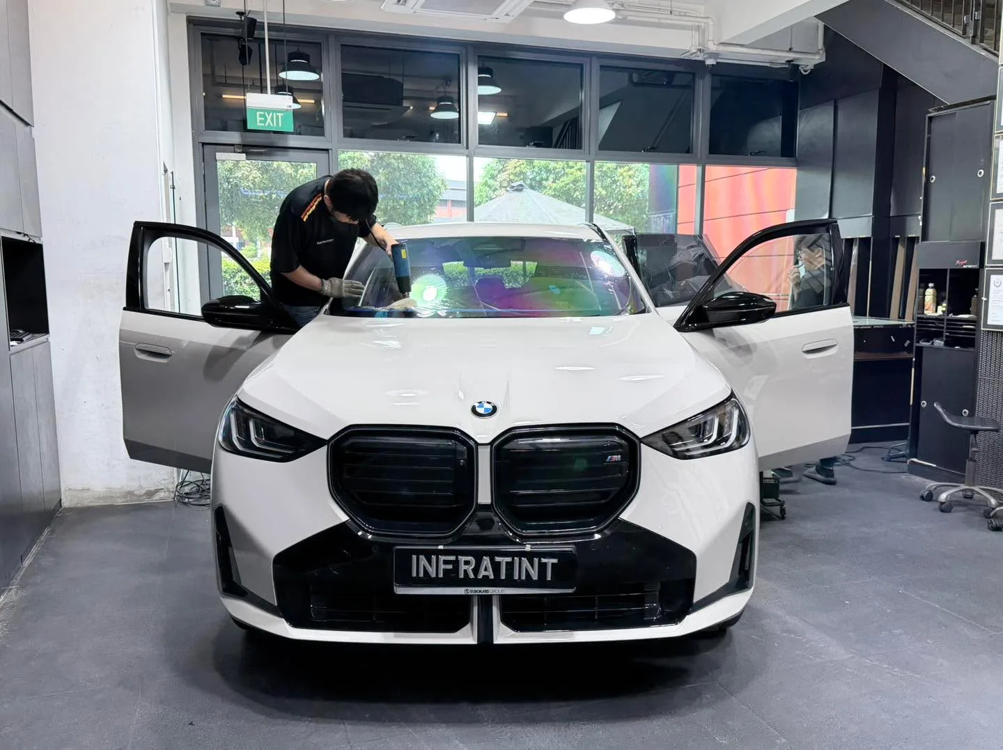 A white BMW sedan with doors open inside the workshop, with staff applying window film.