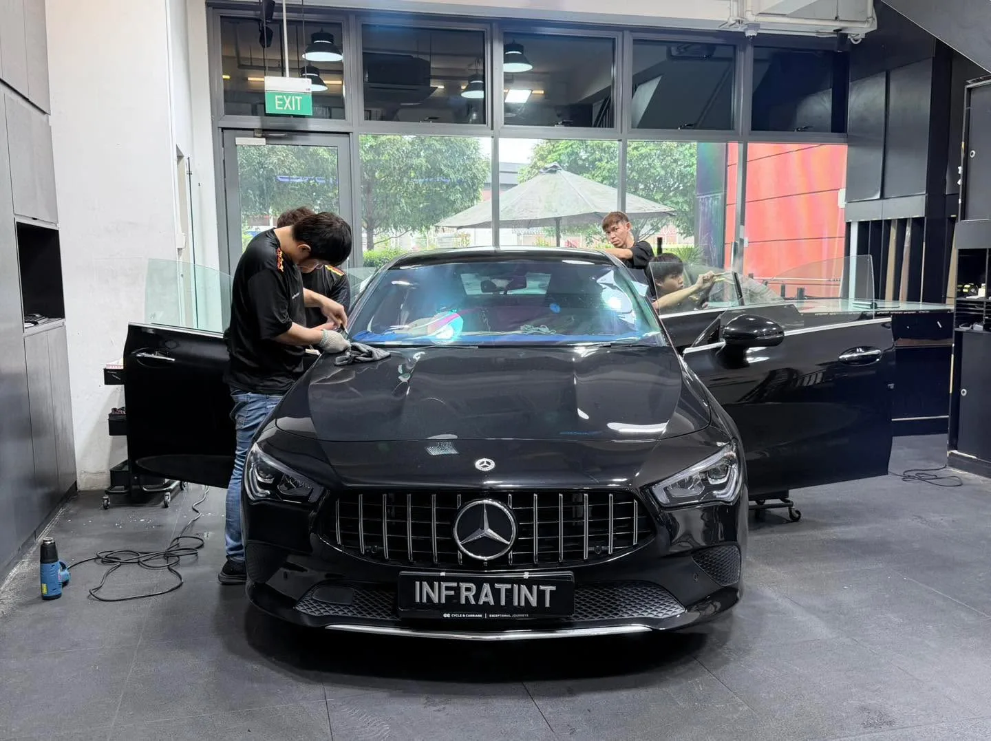 A black Mercedes-Benz sedan with doors open and staff working on the windows inside the facility.