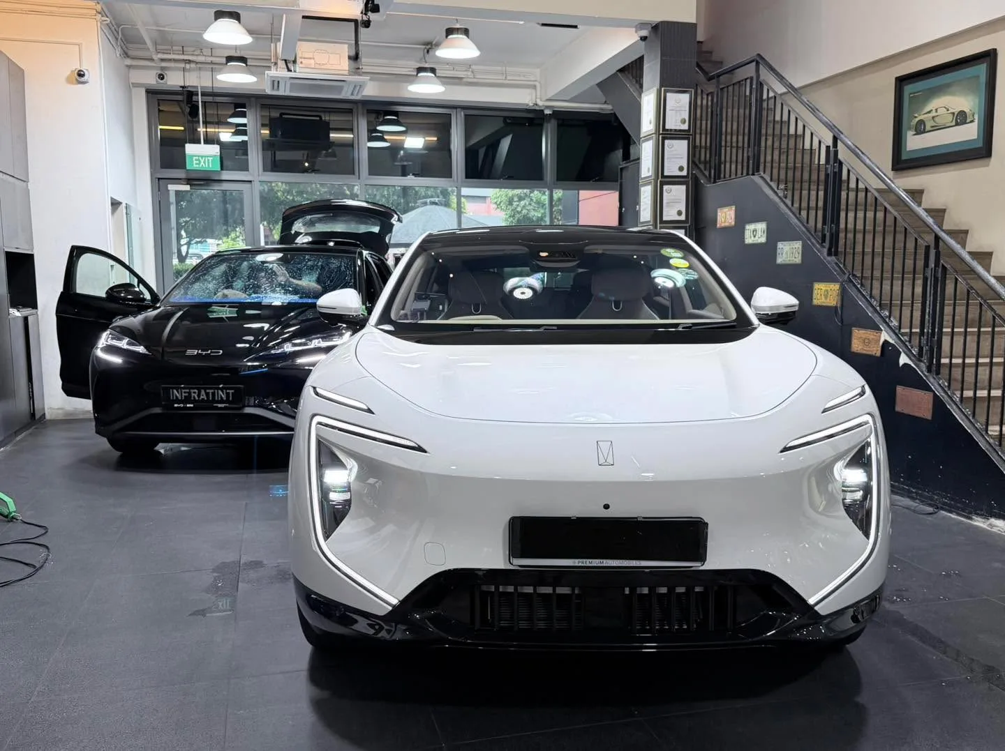 A white Avatr electric sedan and a black Avatr electric sedan parked in an interior workshop space with stairs visible.