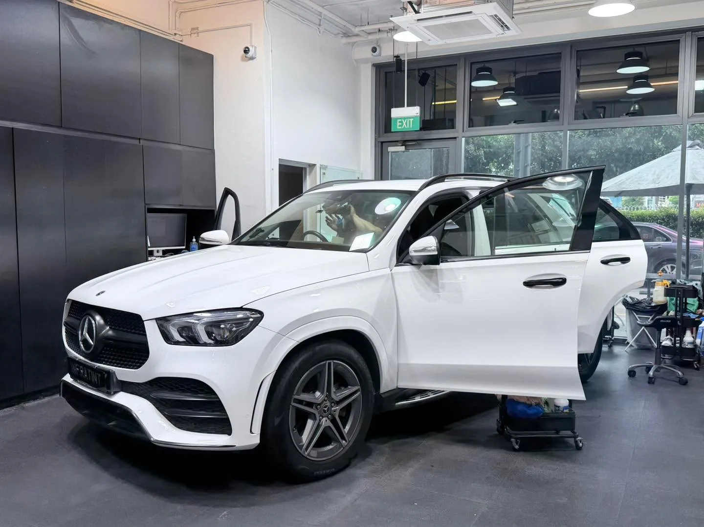 A white Mercedes-Benz GLE 450 compact SUV with its door open, a technician working inside the workshop.