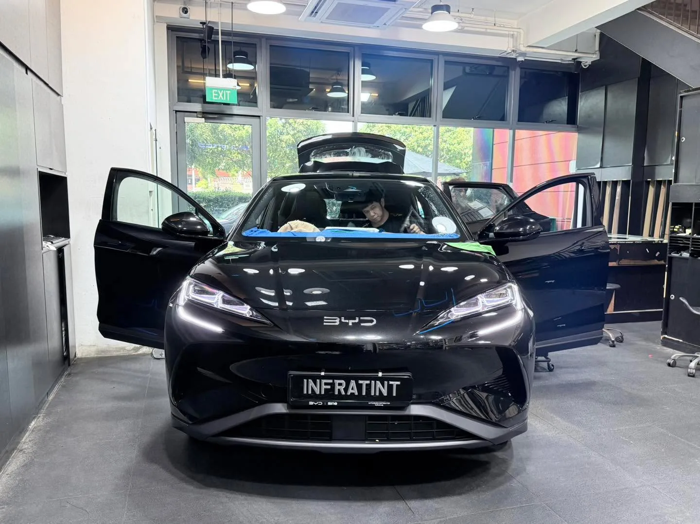 A black Zeekr electric sedan with both doors open, parked in the workshop with staff working on it.