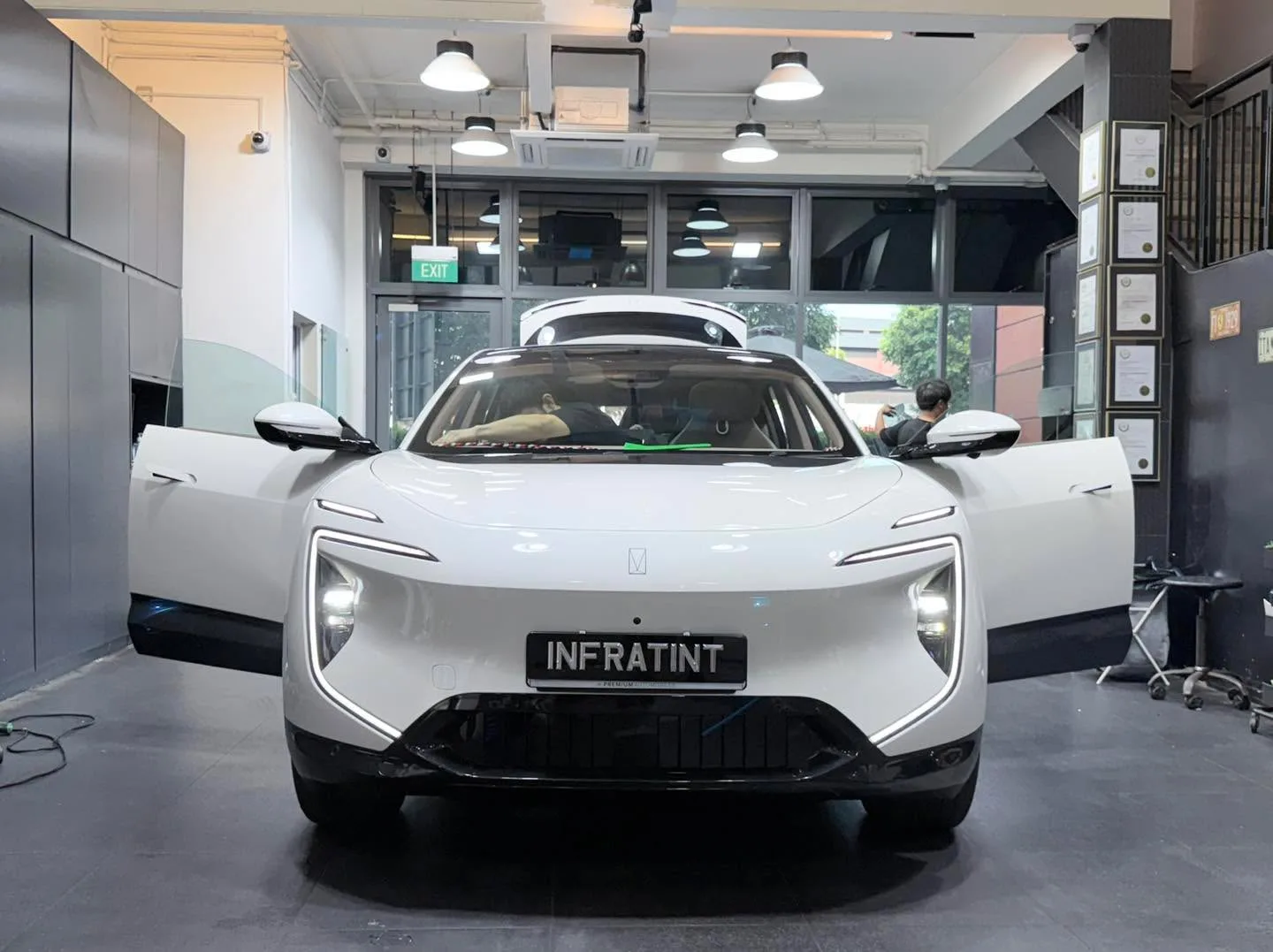 A white BYD Sealion 7 electric SUV with its door open, parked in the workshop with staff working.