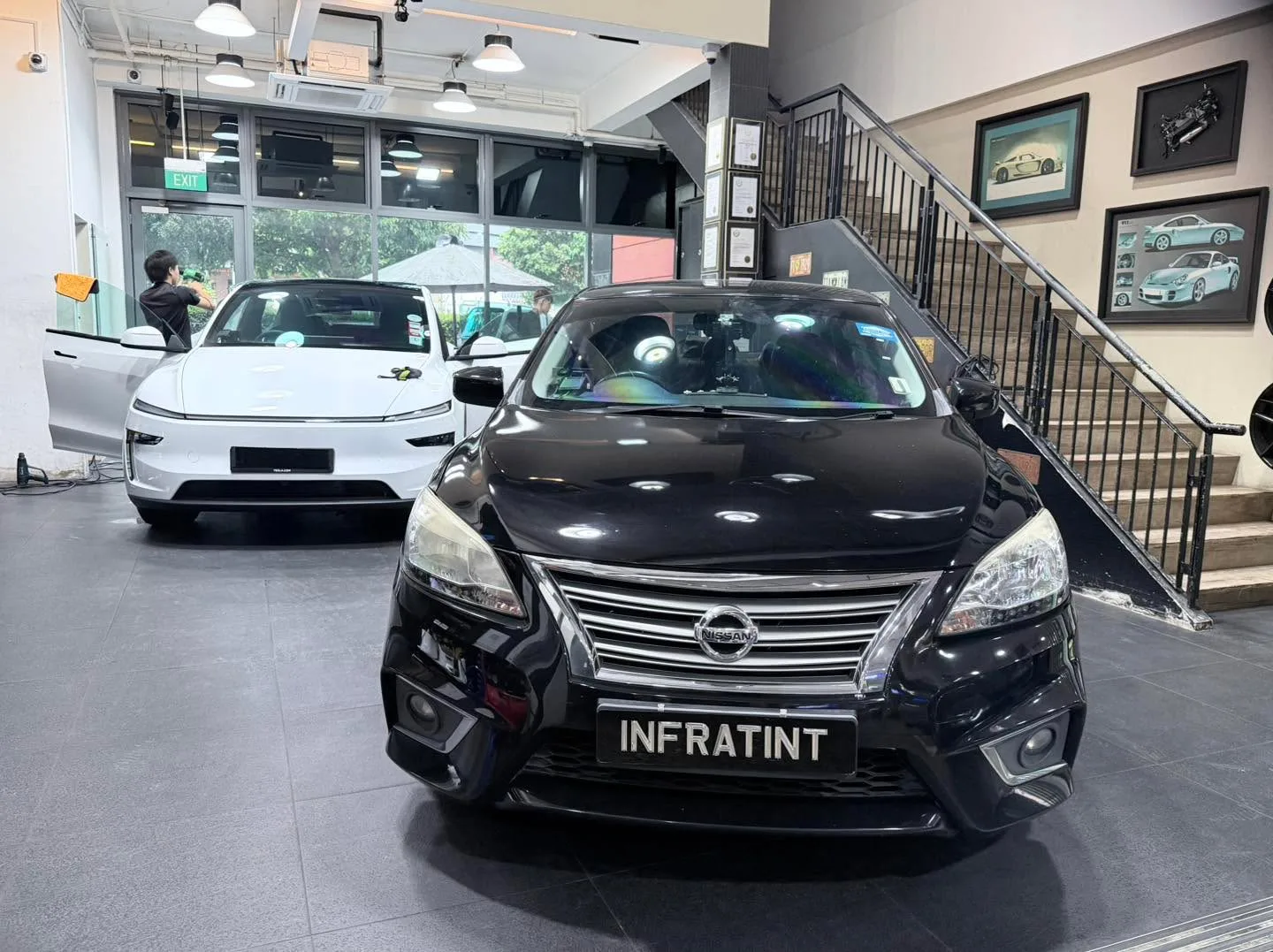 A black Nissan Sylphy with white Tesla Model Y visible in the workshop.