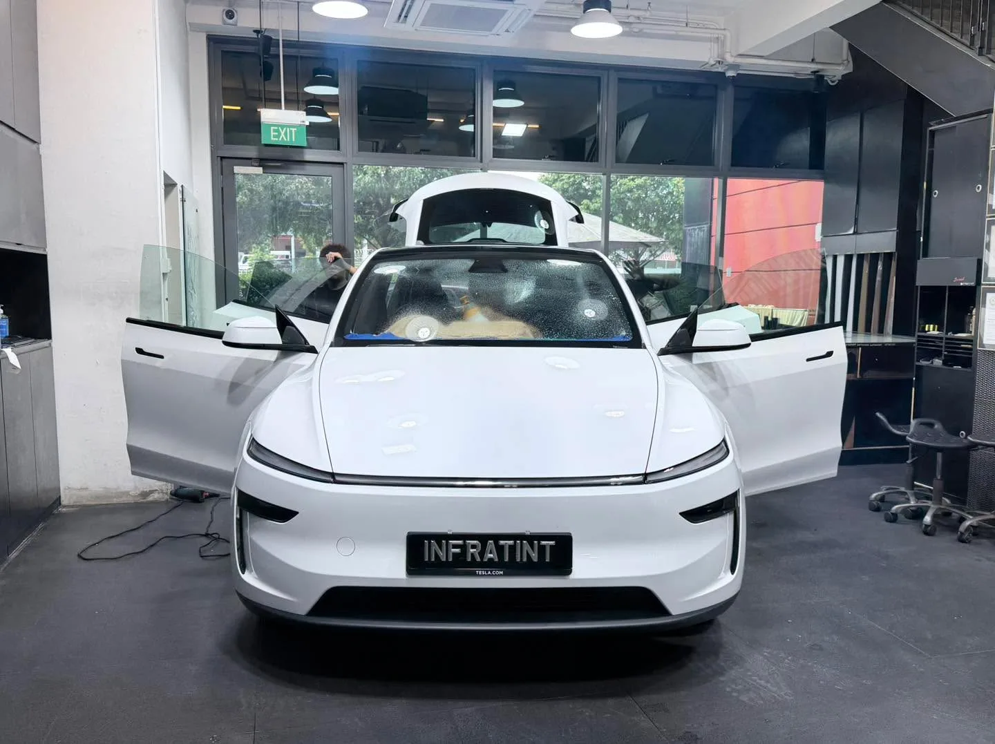 A white Tesla Model Y with open falcon doors in the workshop.