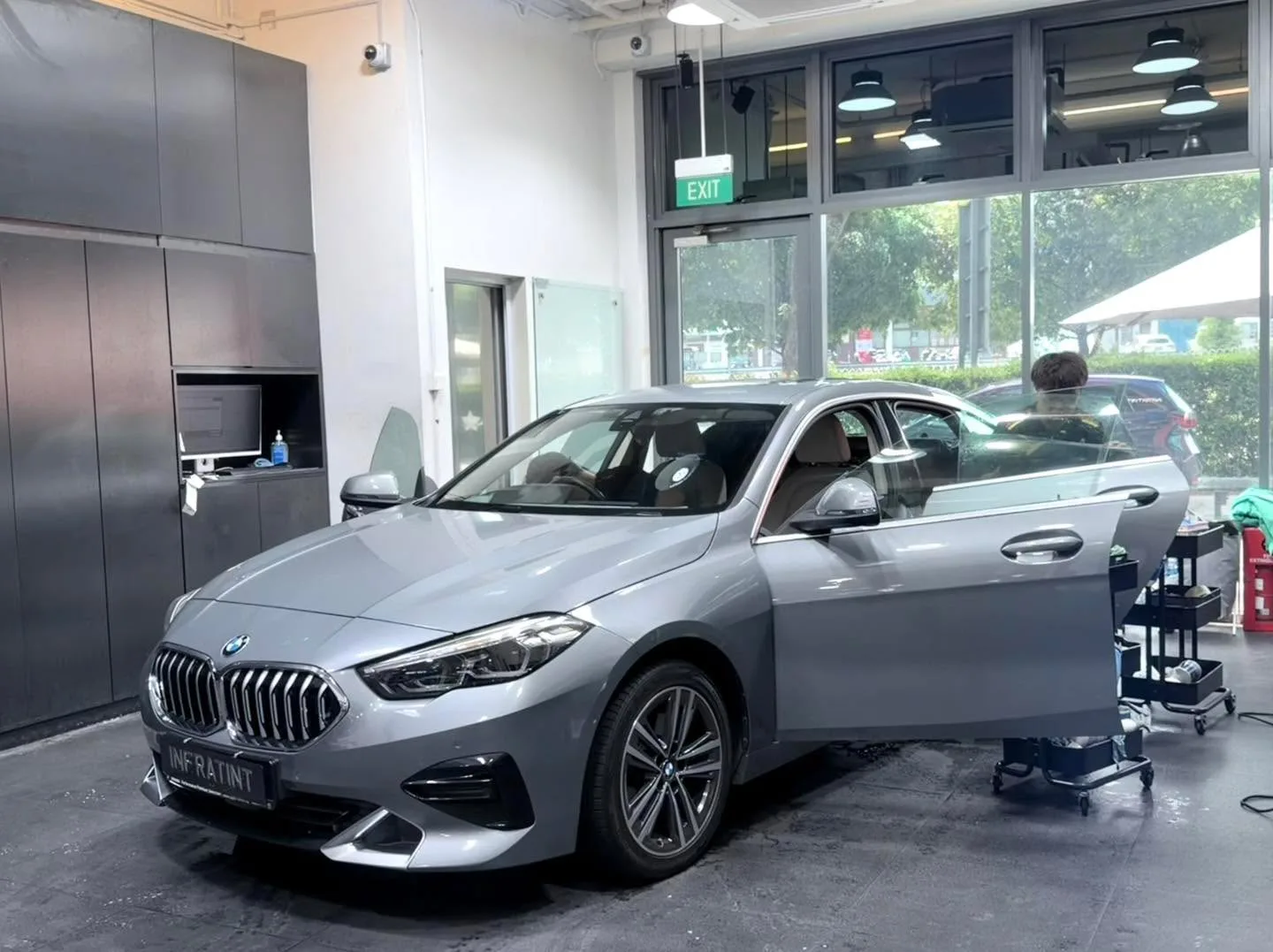 A silver BMW 2 Series being tinted with staff working on the windows.