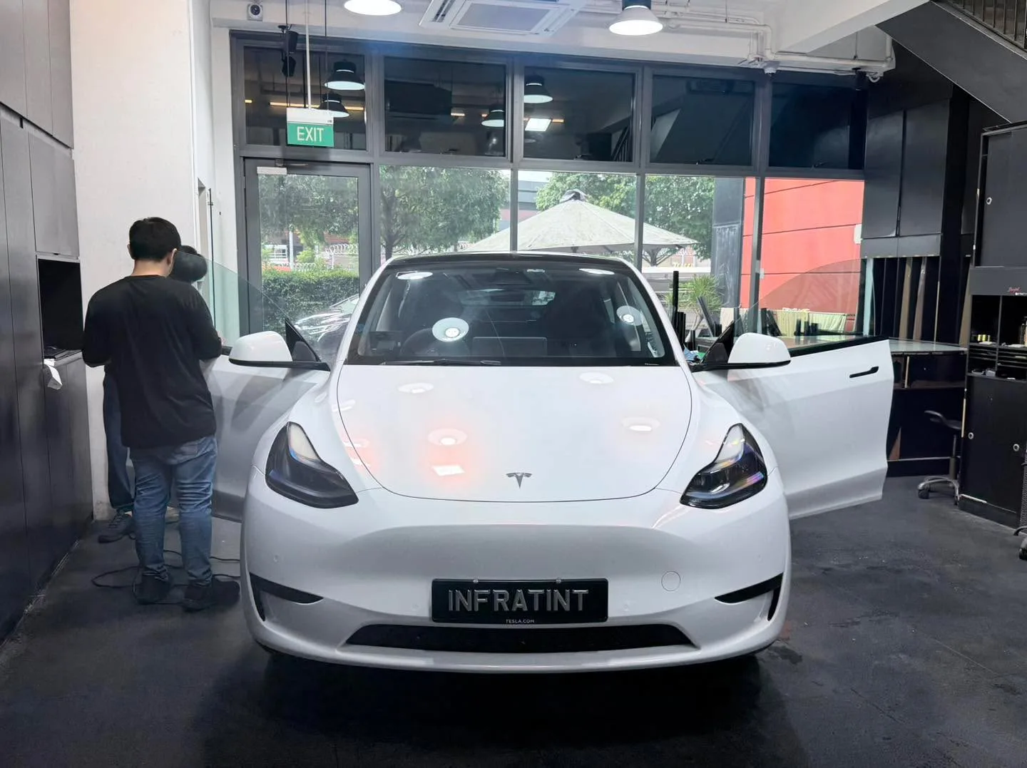 A white Tesla Model Y with open doors during the tinting process.