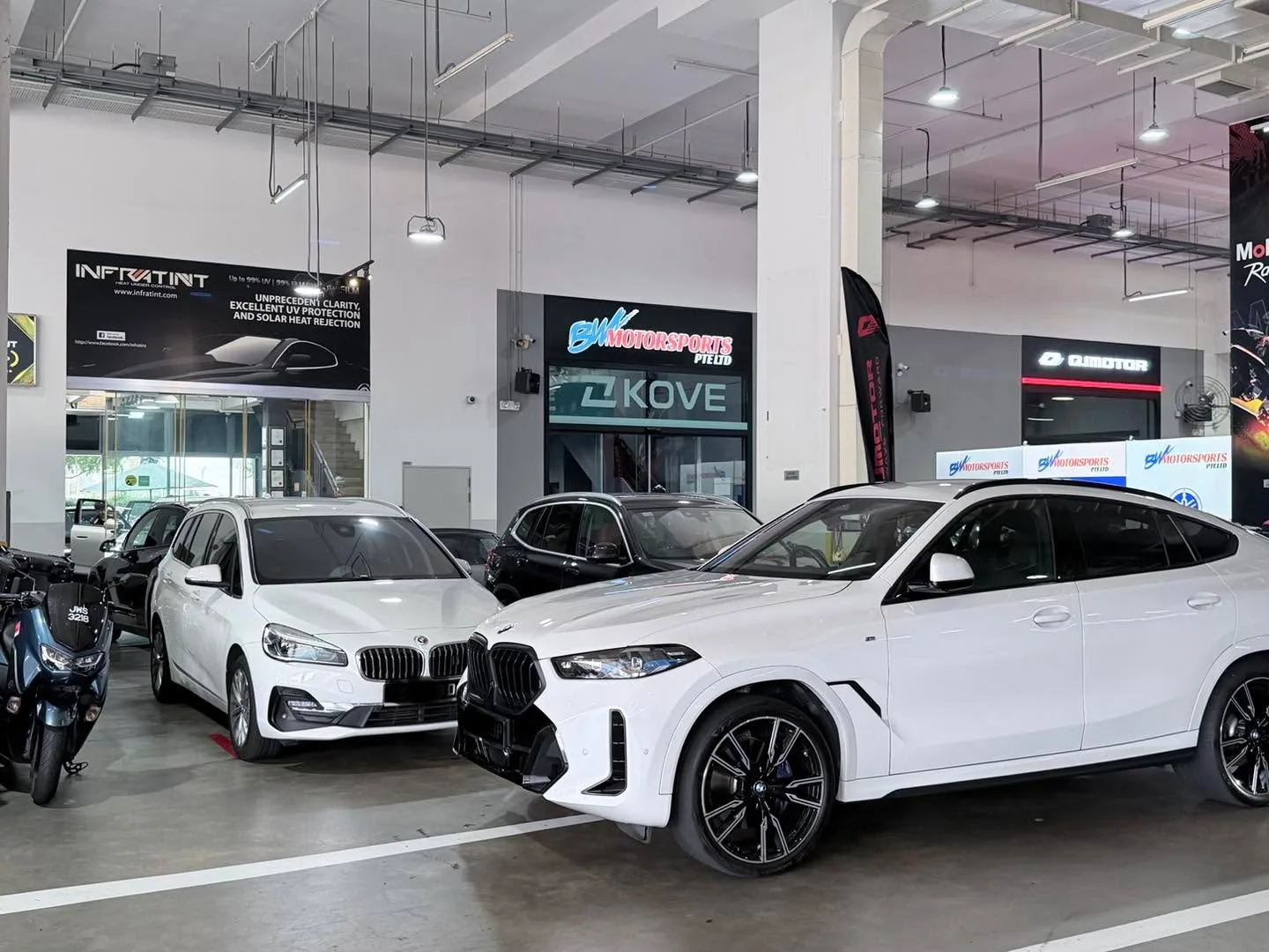 Two white BMW SUVs and a black car parked side by side in the workshop.