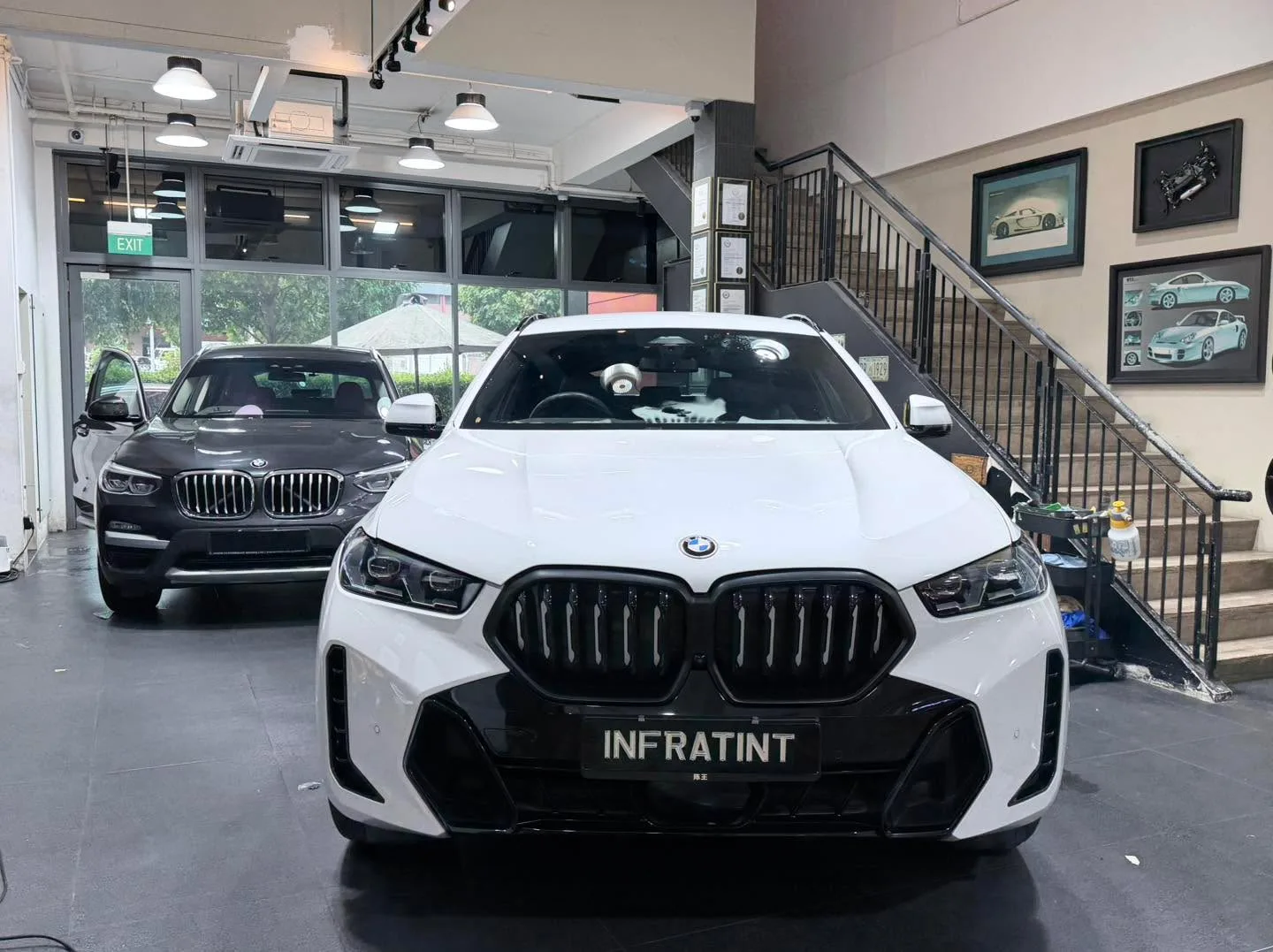 A white BMW X6 and black BMW X3 parked front to back in the workshop.