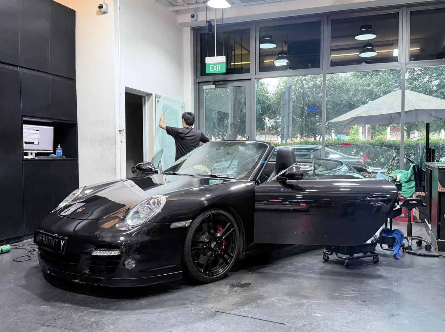 A black Porsche 997 convertible with open doors inside the workshop.