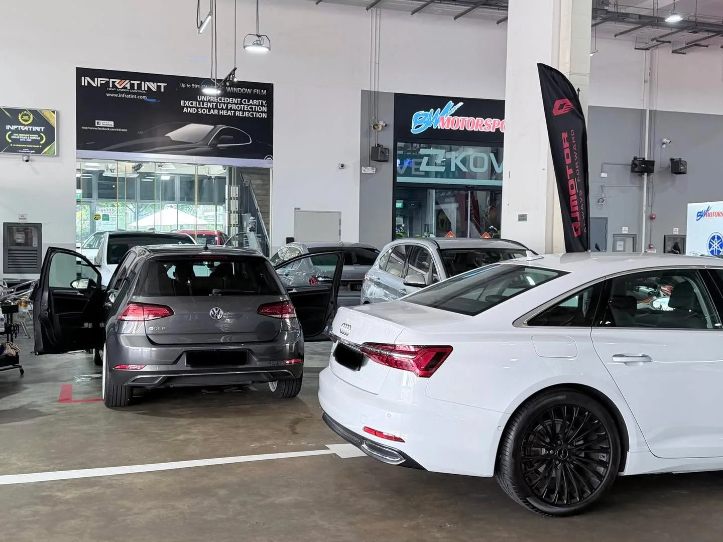 A grey Volkswagen hatchback with its door open and a white Audi sedan at the Infratint workshop.